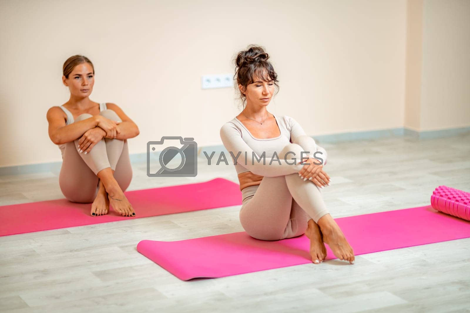 Royalty free image of Fitness, pilates stretching exercises, a group of two attractive smiling mature women in beige sports clothes, train in a sports club. by Matiunina