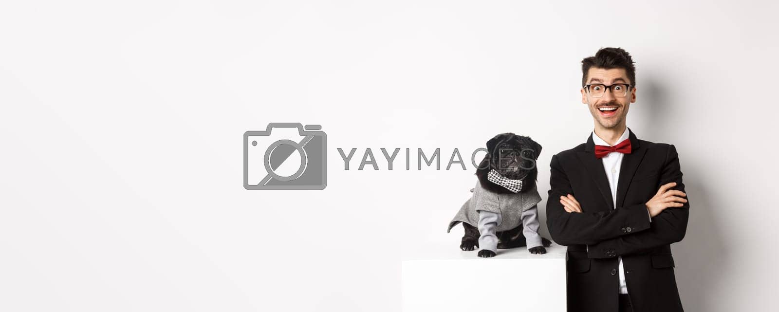 Royalty free image of Animals, party and celebration concept. Happy dog owner in suit and puppy in costume looking excited at camera, having fun, standing over white background by Benzoix