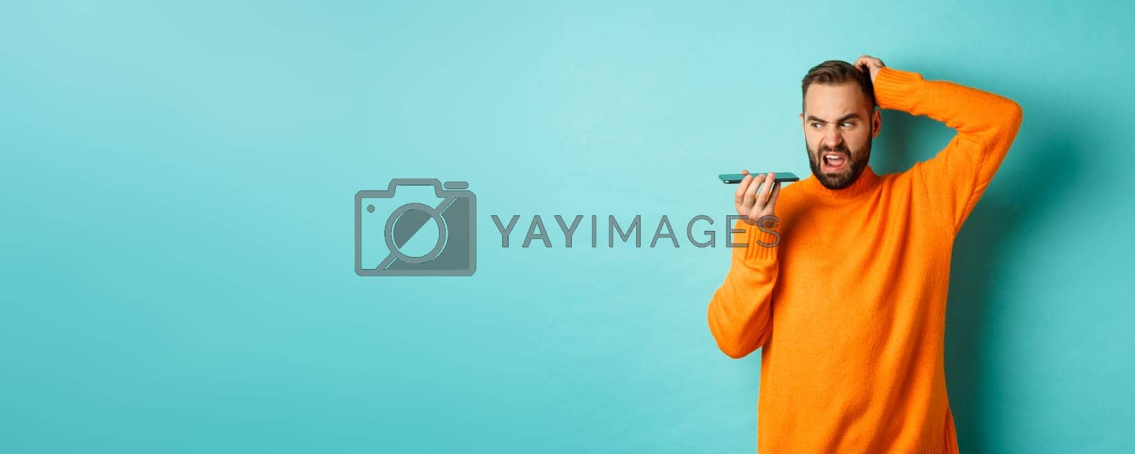 Royalty free image of Confused man scratching head while talking on speakerphone, record voice message with indecisive face, standing in orange sweater over light blue background by Benzoix