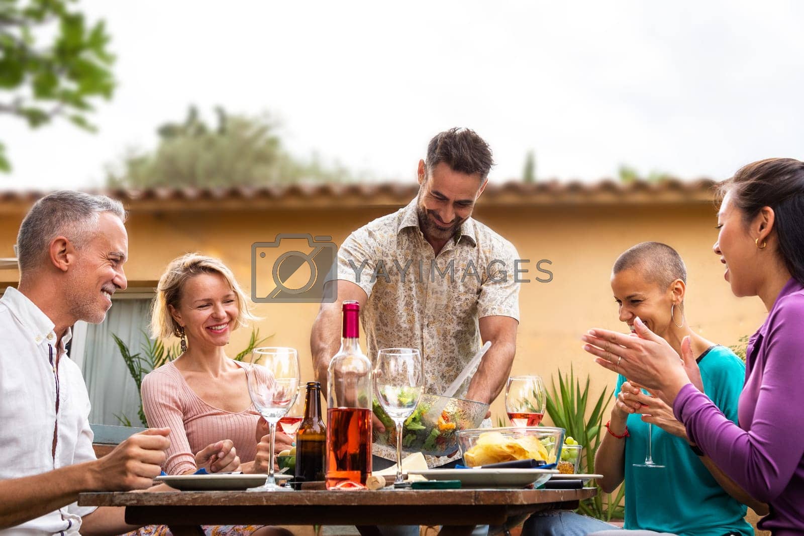 Royalty free image of Man serving food to friends during outdoor garden dinner party. Friends having fun. by Hoverstock