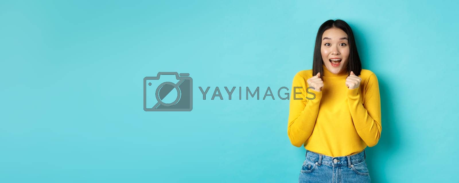 Royalty free image of Hopeful and happy asian woman looking with amazement and hope at camera, winning, standing over blue background by Benzoix