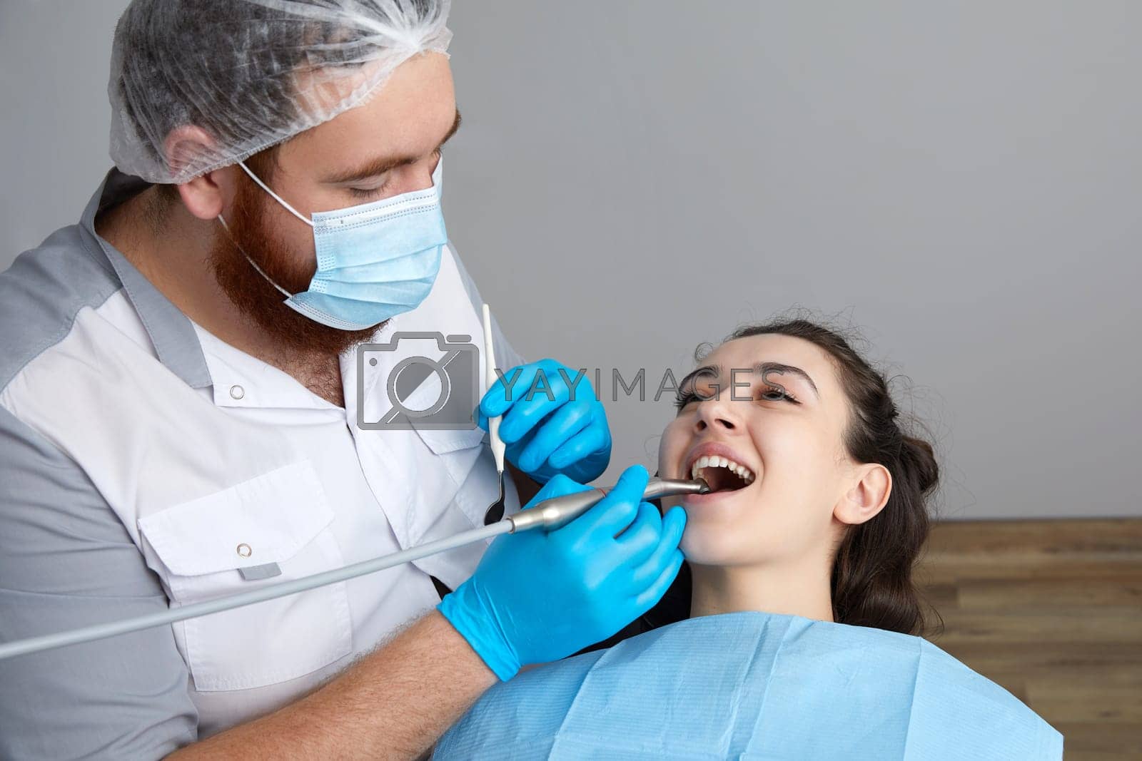 Royalty free image of Dentist drilling tooth of female patient in dental chair by Mariakray