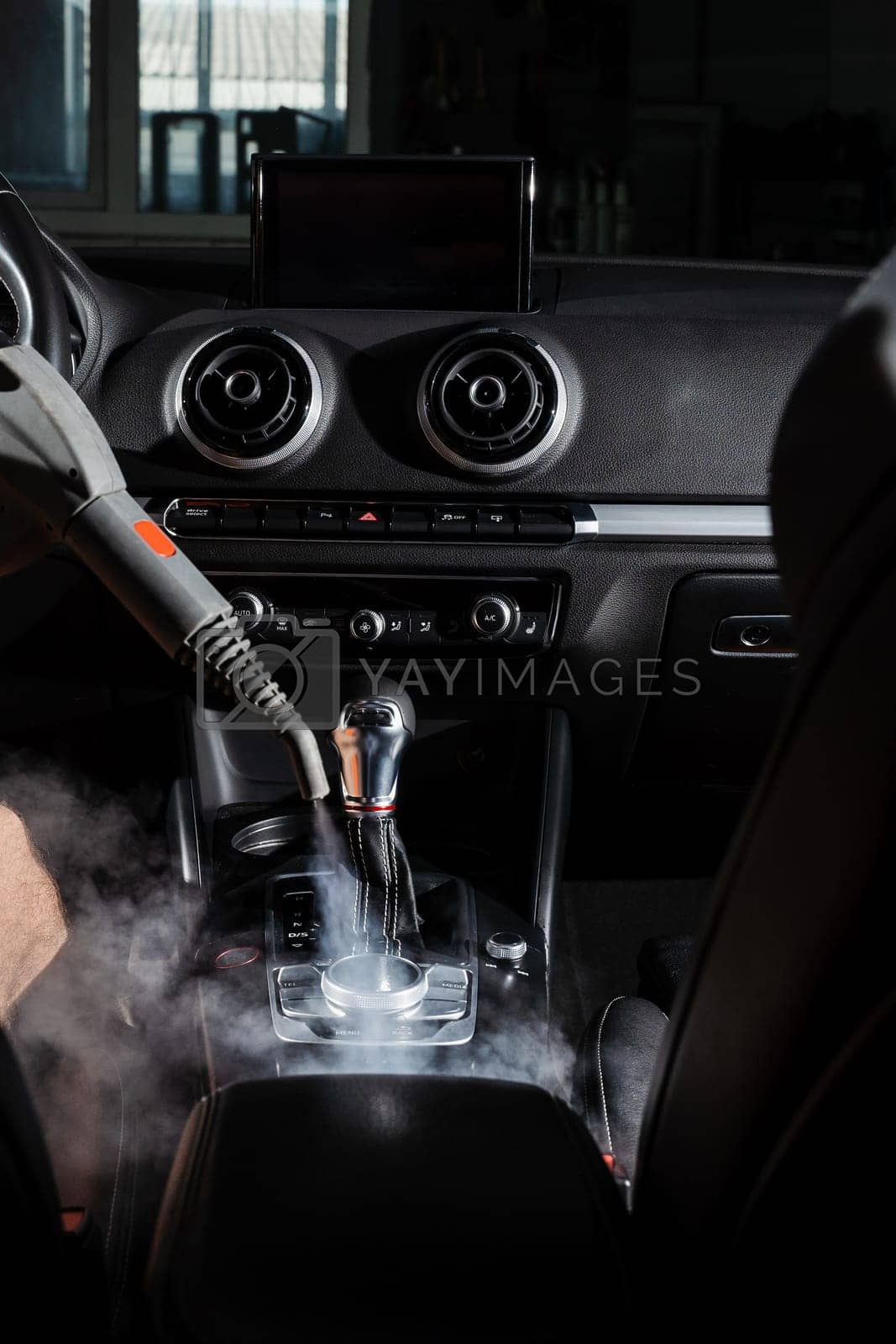 Royalty free image of Steam cleaning of gearbox and dashboard in car. Vaping steam. Cleaning individual elements of black leather interior in auto. Creative advert for auto detailing service. by Rabizo