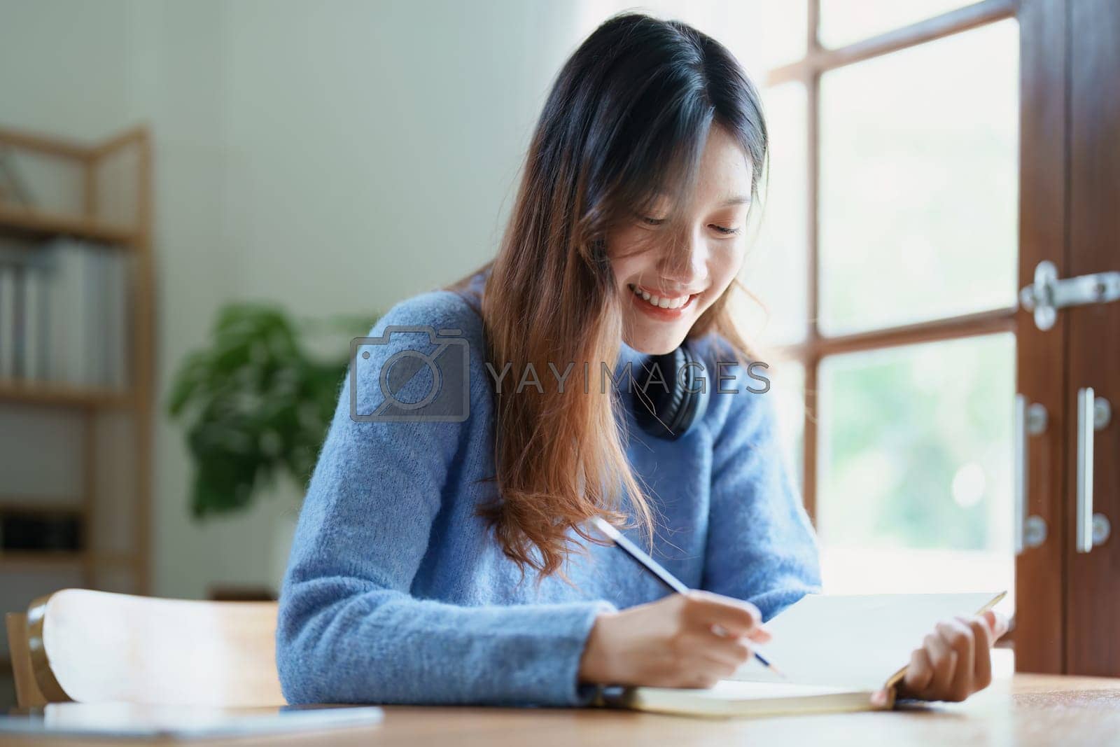 Royalty free image of Portrait of a teenage Asian woman using a notebook to study online via video conferencing on a wooden desk at home by Manastrong