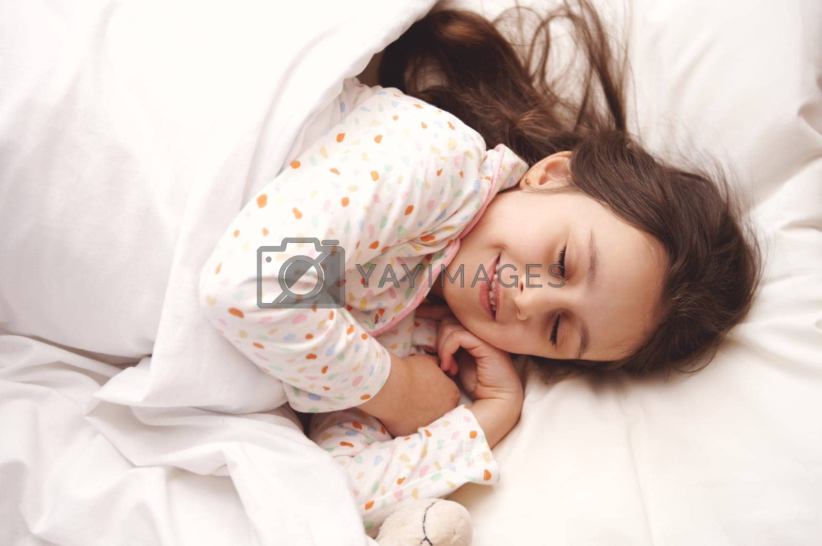 Royalty free image of View from above of a Caucasian beautiful little child girl in white pajamas, taking a nap in a white sunny bedroom by artgf