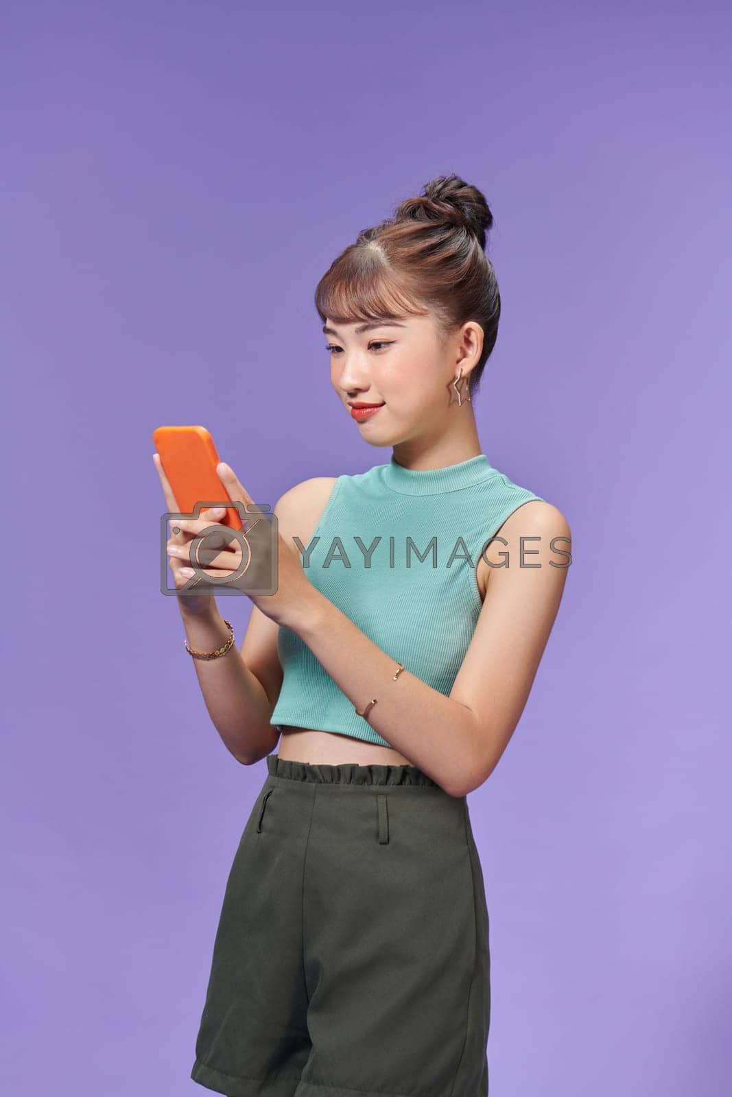 Royalty free image of Pretty millennial girl isolated on purple background text messaging on cell phone by makidotvn