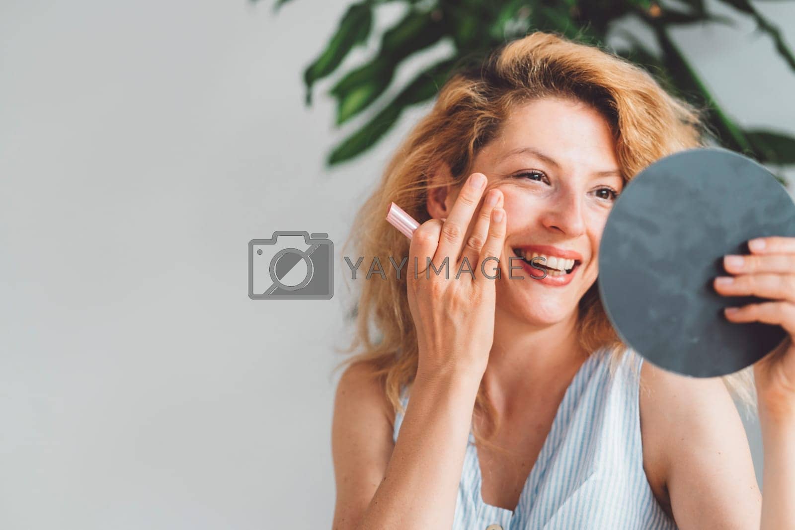 Royalty free image of Smiling woman doing her make up looking at her self in a mirror she is holding up by VisualProductions