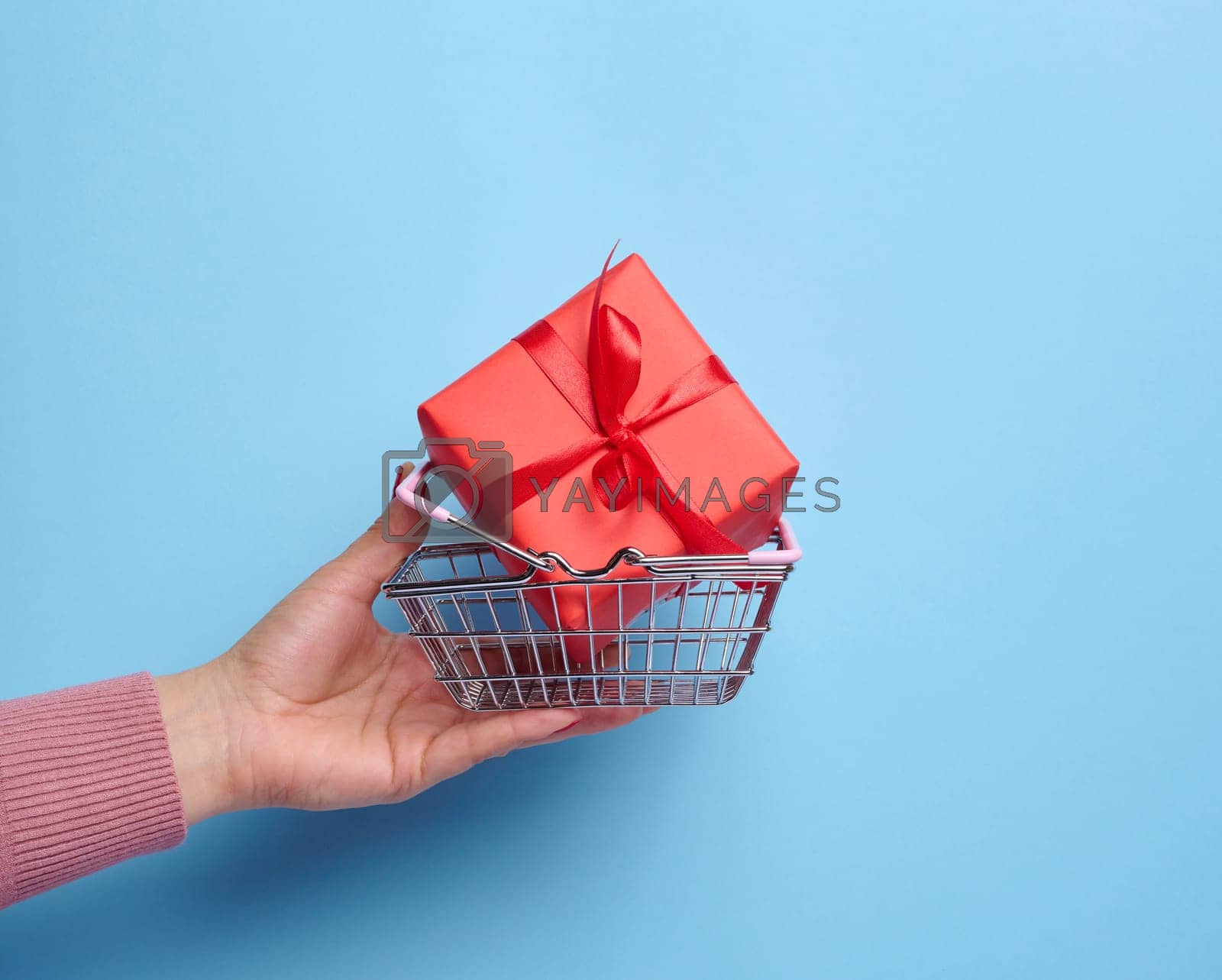 Royalty free image of A woman's hand holds a red gift box wrapped in mid-air against a blue background, concept of celebration, surprise by ndanko