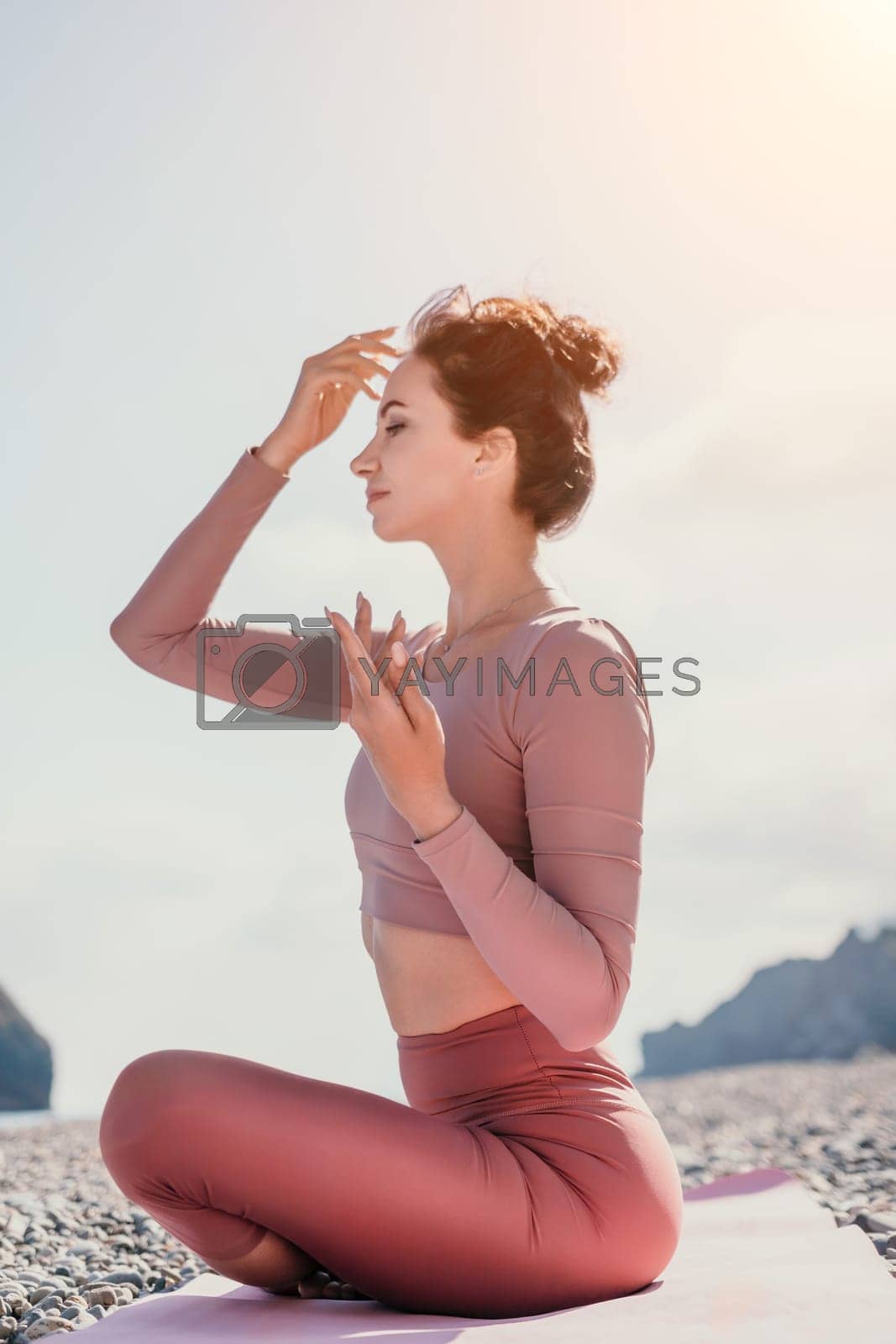 Royalty free image of Middle aged well looking woman with black hair, fitness instructor in leggings and tops doing stretching and pilates on yoga mat near the sea. Female fitness yoga routine concept. Healthy lifestyle by panophotograph