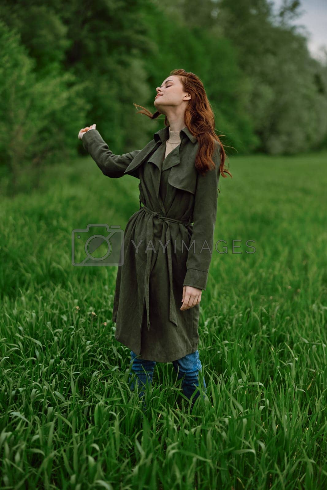 Royalty free image of a woman in a long raincoat stands in tall green grass in a field in rainy weather in spring by Vichizh