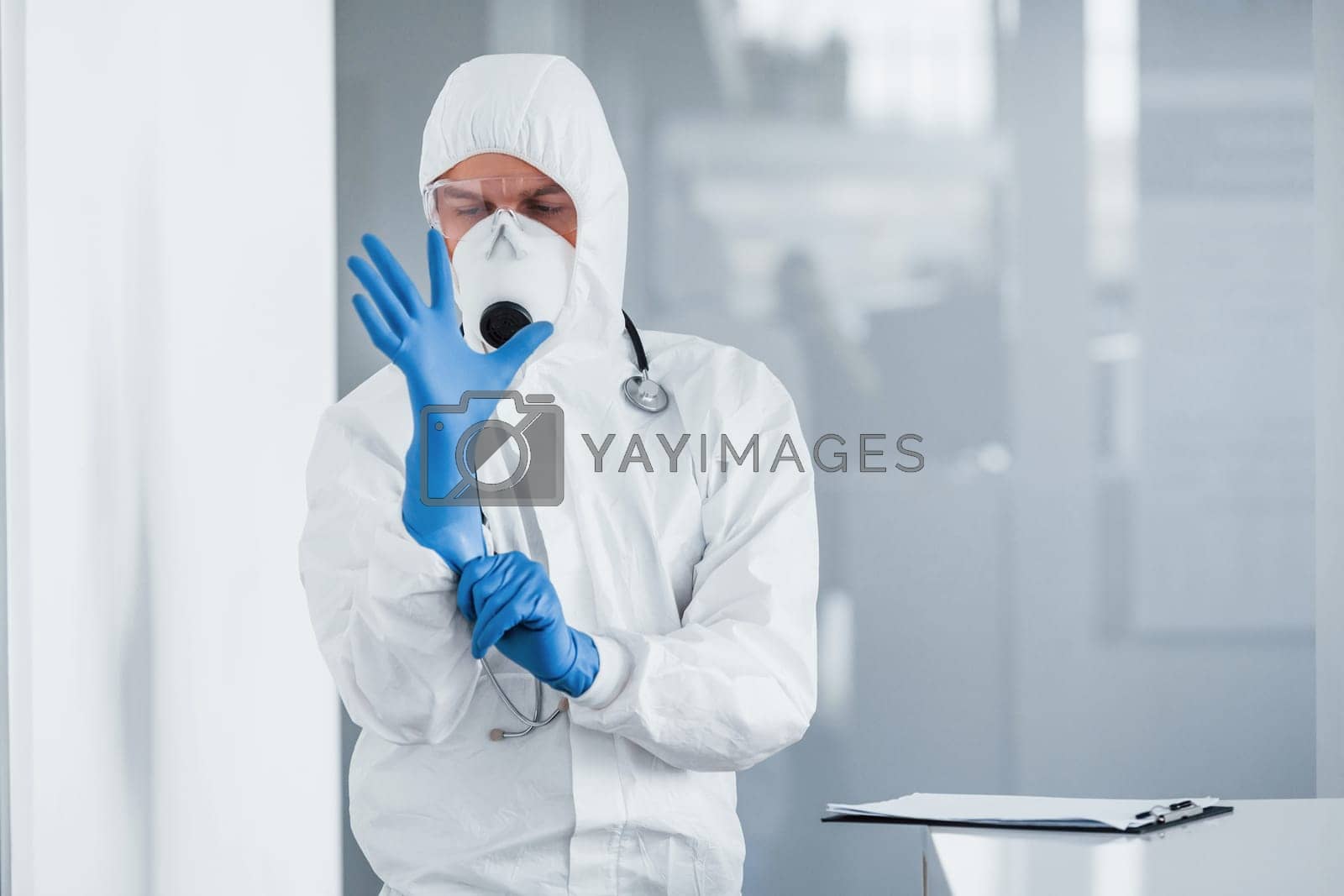 Royalty free image of Male doctor scientist in lab coat, defensive eyewear and mask wearing blue gloves by Standret