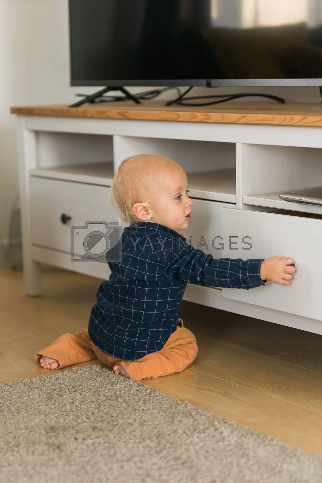 Royalty free image of Toddler baby boy open cabinet drawer with his hand. Child explore what is in cabinet. Baby curiosity and child development stages by Satura86