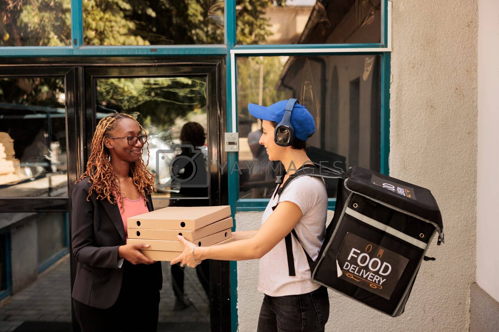 Royalty free image of African american smiling office worker receiving pizza order outdoors by DCStudio