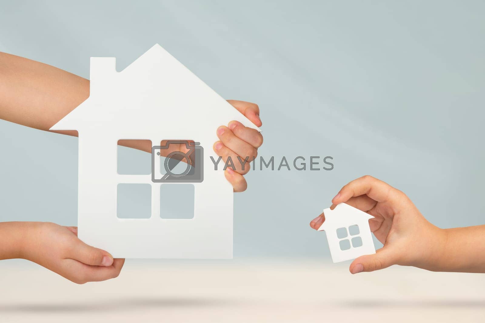 Royalty free image of Choice between big or small house. Buying property, property comparison before buying. Model of a large and small white house in the hands on a blurred background. Buy a house or apartment. by SERSOL