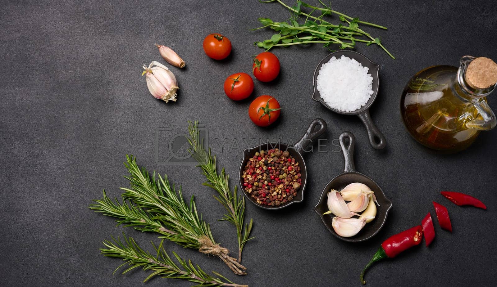 Royalty free image of Miniature pans with spices, salt, black pepper and fragrant pepper, a sprig of rosemary on a black table. Spices for cooking by ndanko