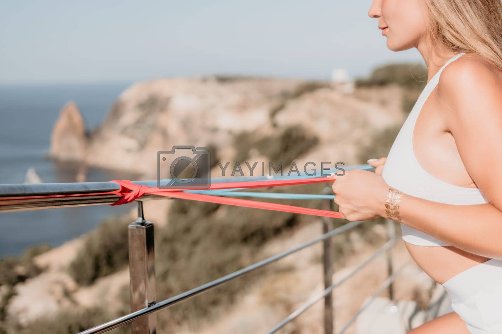 Royalty free image of Fitness woman sea. Outdoor workout with fitness rubber bands in park over beach. Female fitness yoga routine concept. Healthy lifestyle. Happy fit woman exercising with rubber band in park. by panophotograph