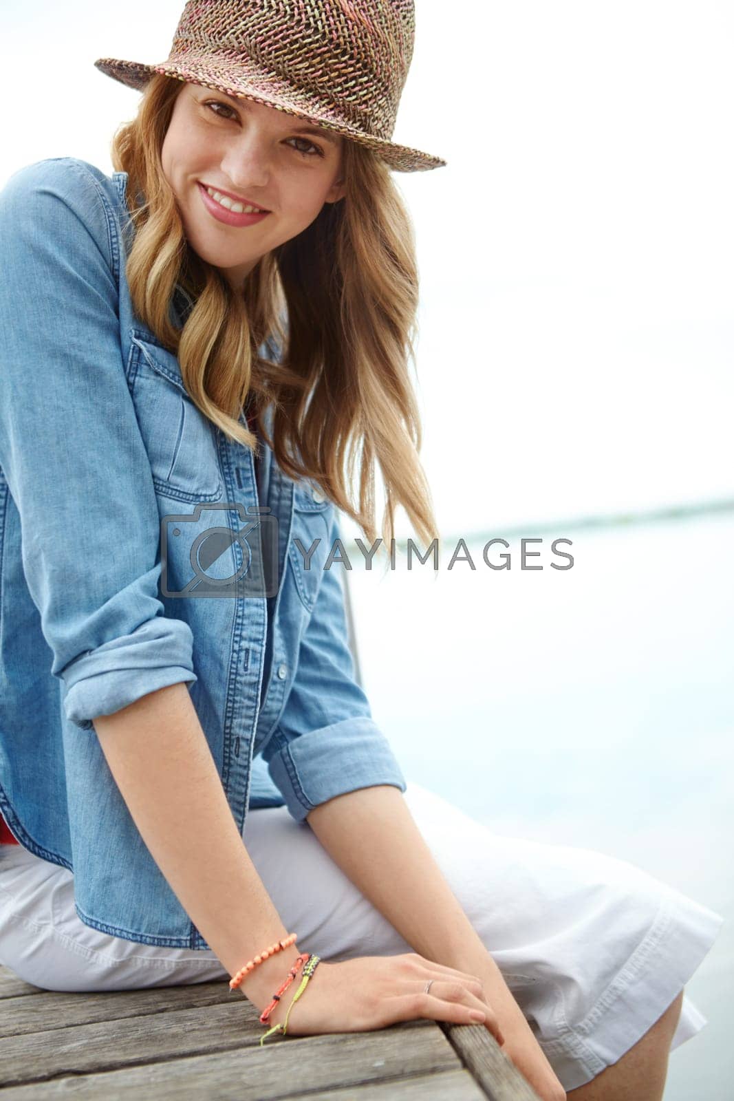 Royalty free image of Tranquility by the lake. A happy young woman sitting on a jetty next to a lake. by YuriArcurs