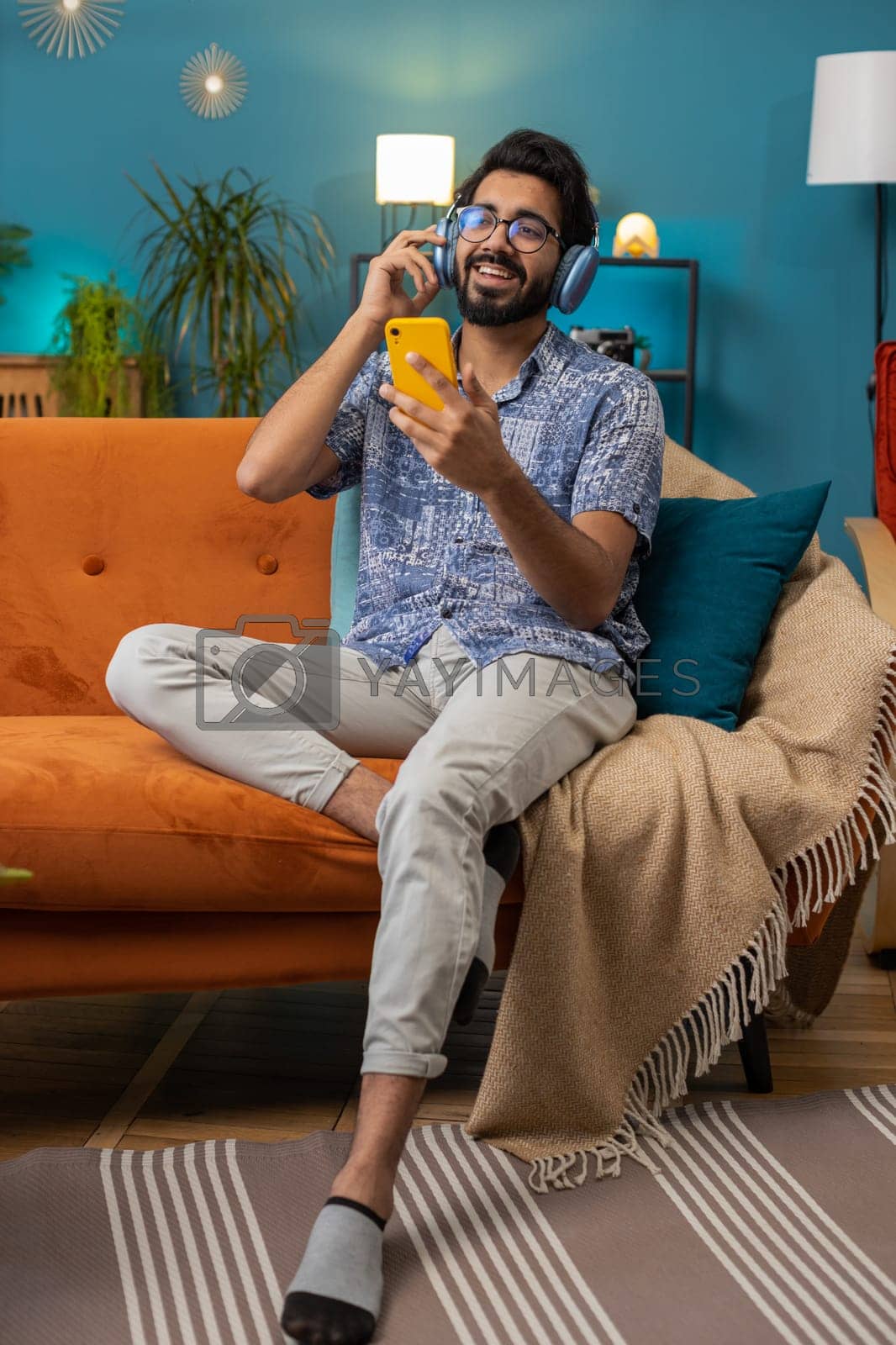Royalty free image of Happy indian man in wireless headphones relaxing sitting on sofa at home listening favorite music by efuror