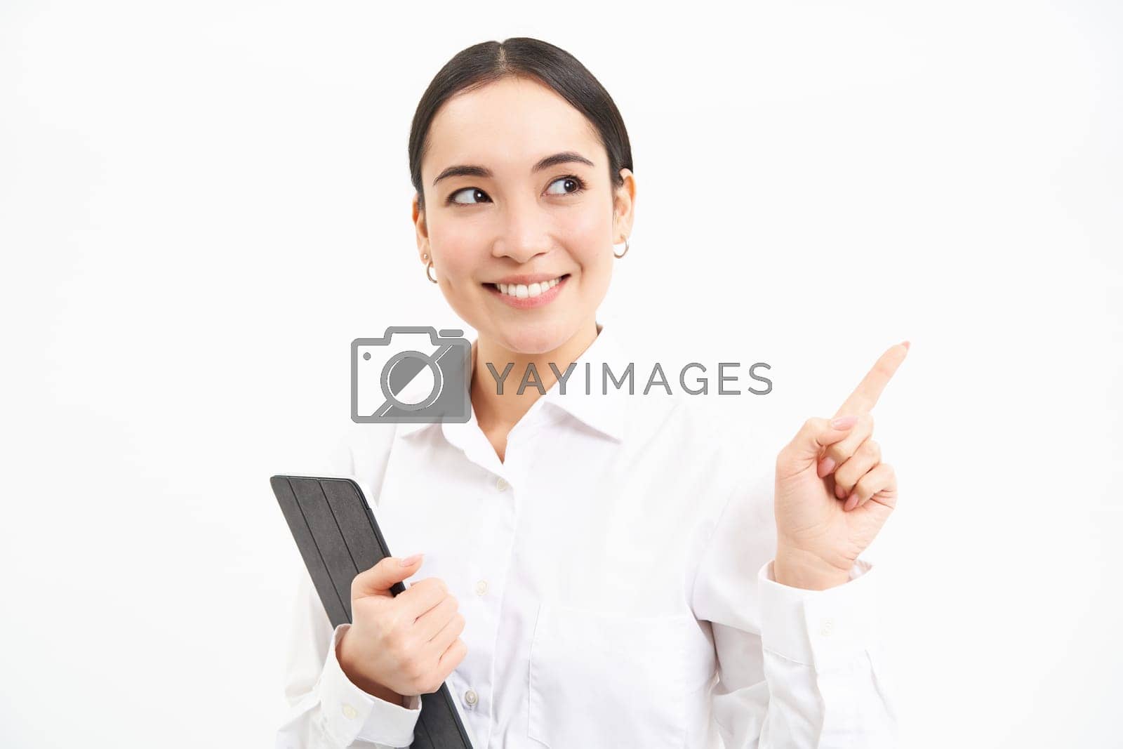 Royalty free image of Image of young professional woman, pointing finger right, holding digital tablet, showing advertisement campaign, isolated on white background by Benzoix