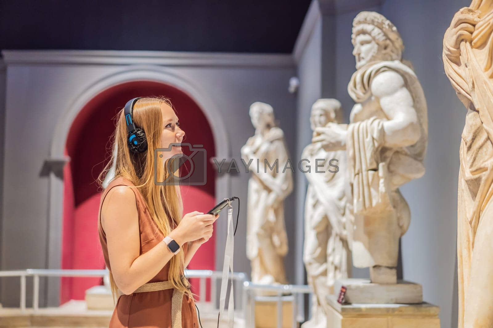 Royalty free image of Portrait of contemporary young woman looking at sculptures and listening to audio guide at museum exhibition by galitskaya
