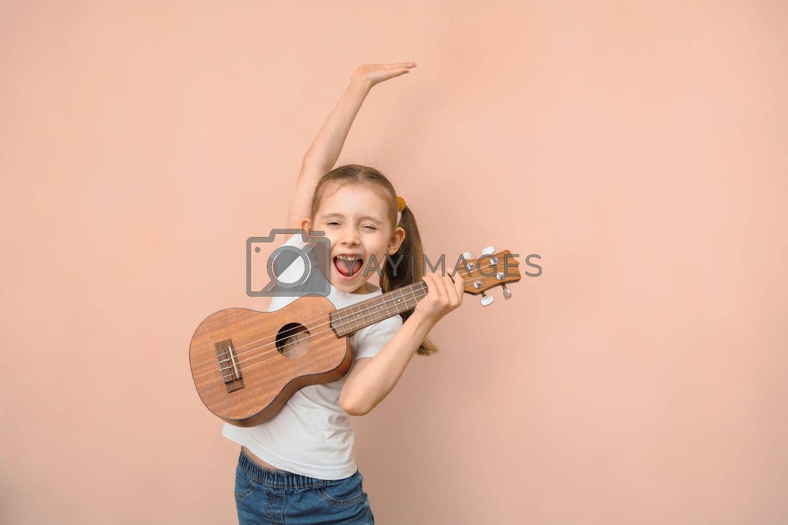 Royalty free image of Expressive emotional Caucasian girl of primary school age learns music by playing the children's guitar by Rom4ek