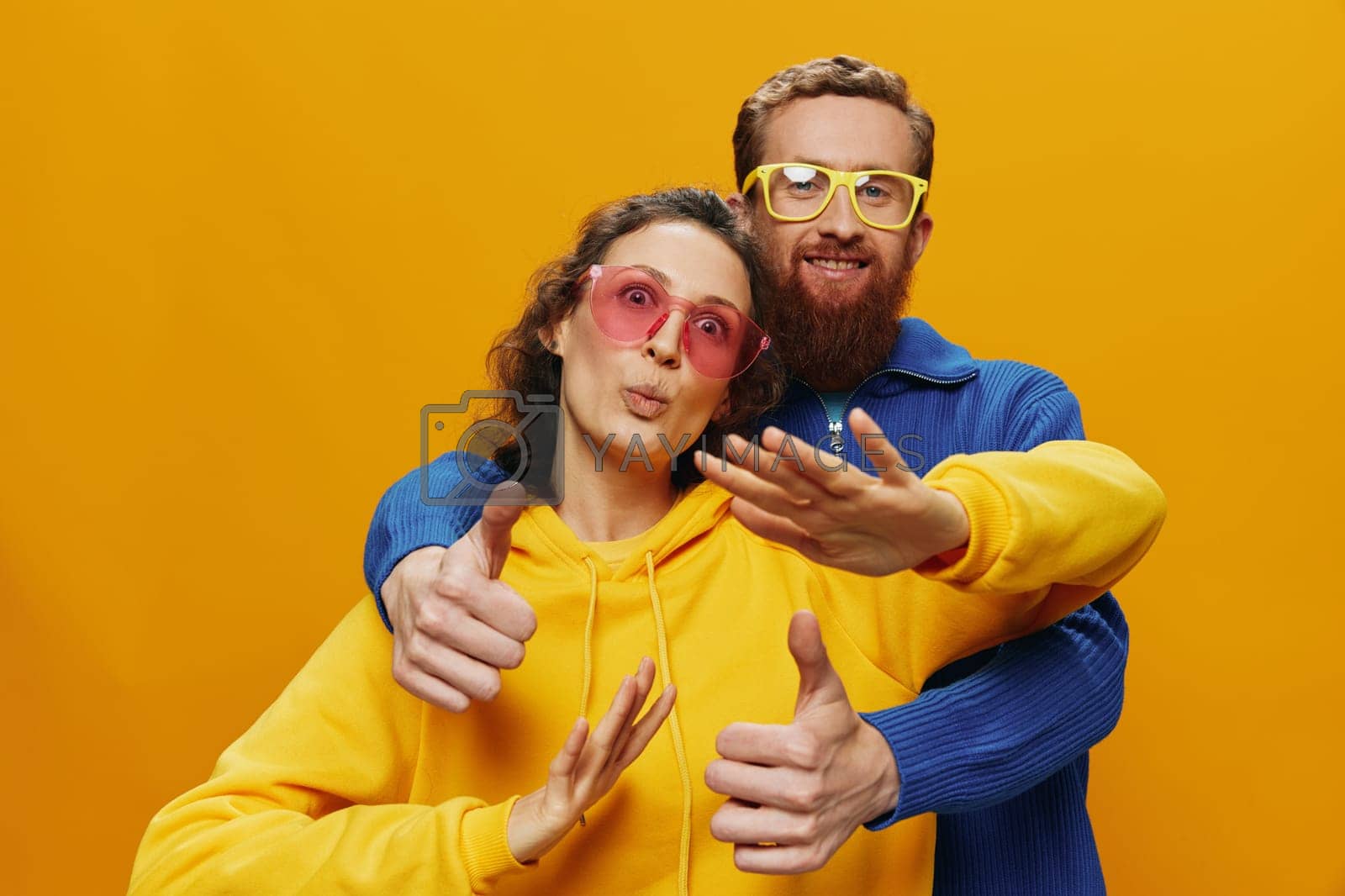 Royalty free image of Man and woman couple smiling cheerfully and crooked with glasses, on yellow background, symbols signs and hand gestures, family shoot, newlyweds. by SHOTPRIME