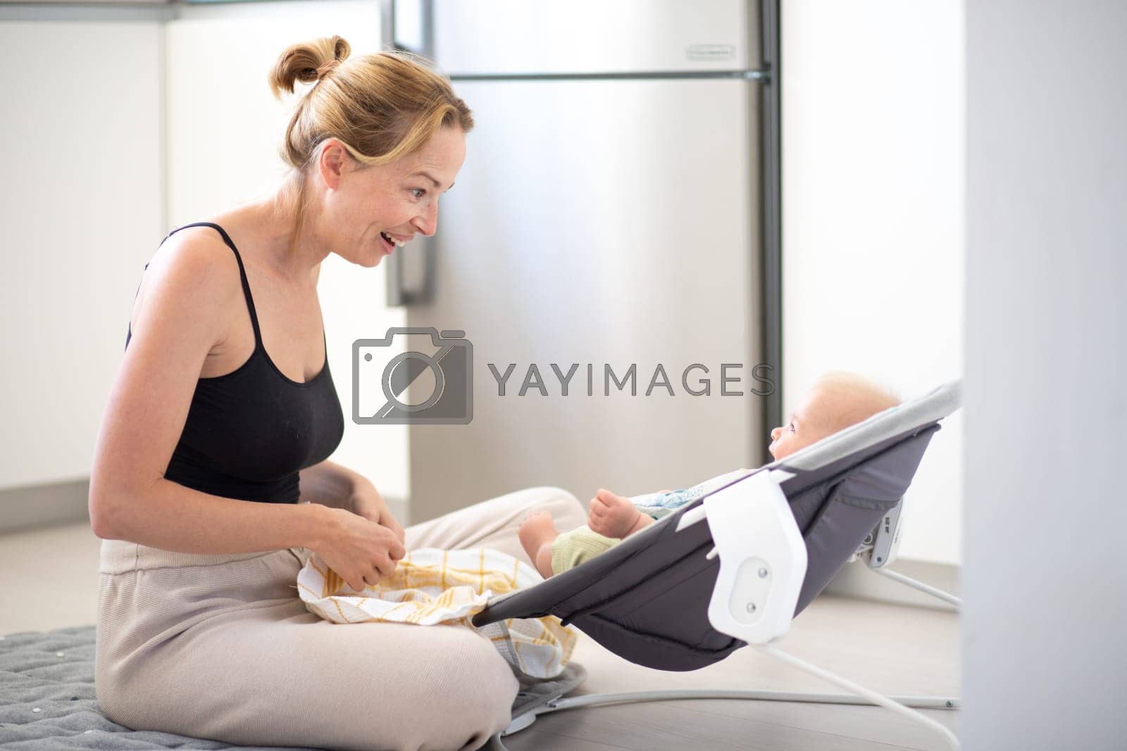 Royalty free image of Happy smiling mother playing with her little baby son sitting in electric rocking chair at home. Child development and happy parenting. by kasto