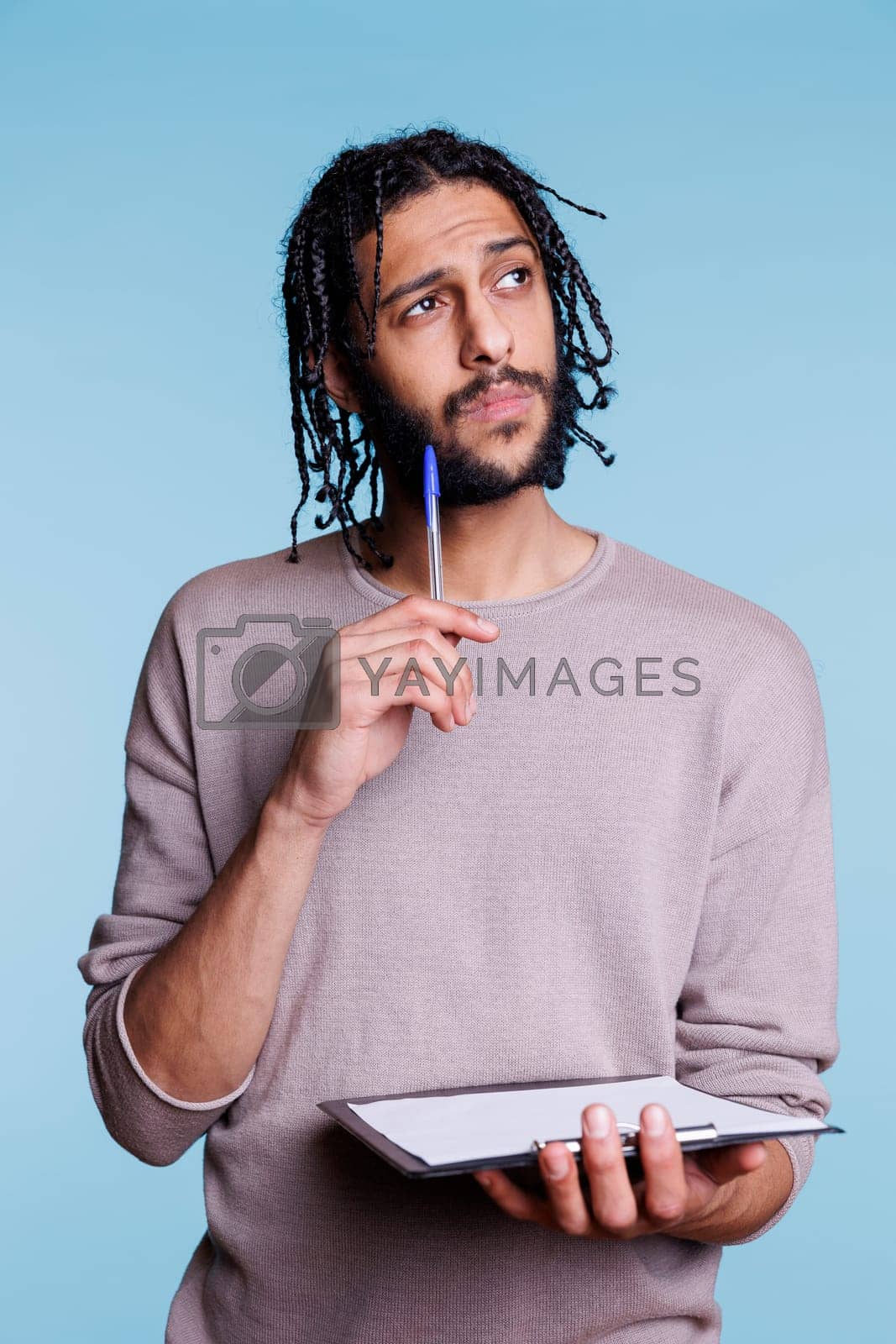 Royalty free image of Puzzled arab man thinking while checking plan on clipboard by DCStudio