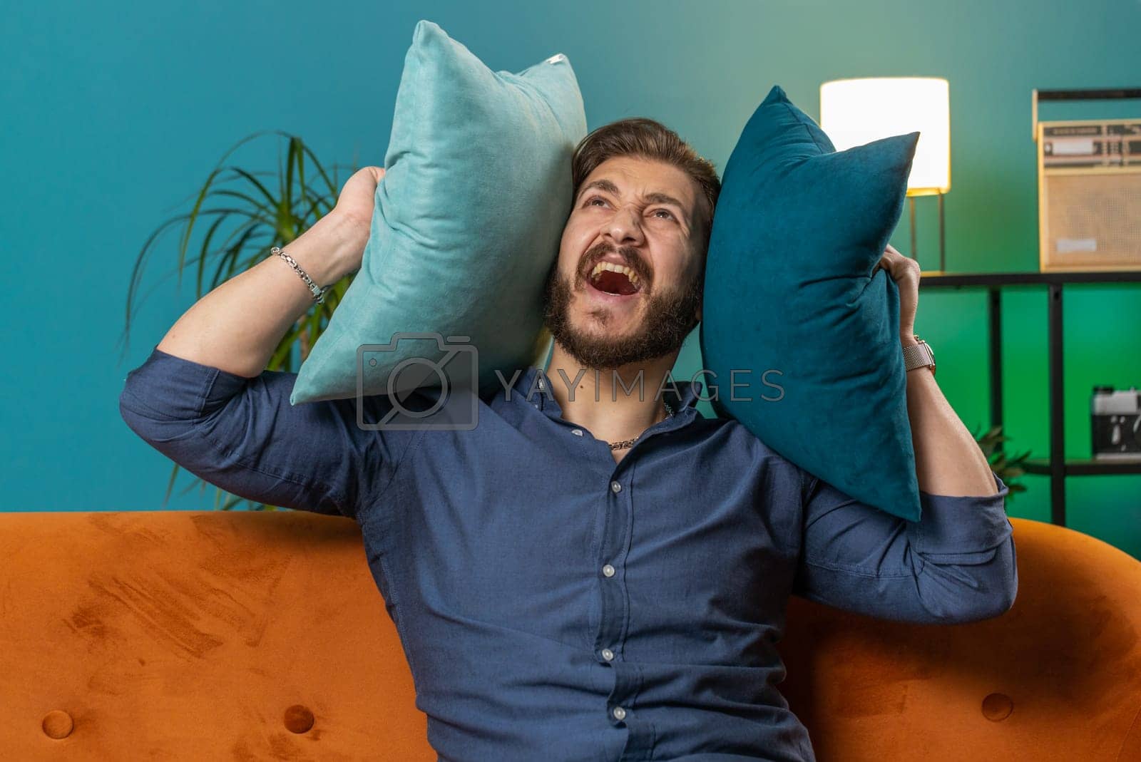 Royalty free image of Repair work at neighbours concept, irritated man at home cover ears with pillows annoyed by noise by efuror