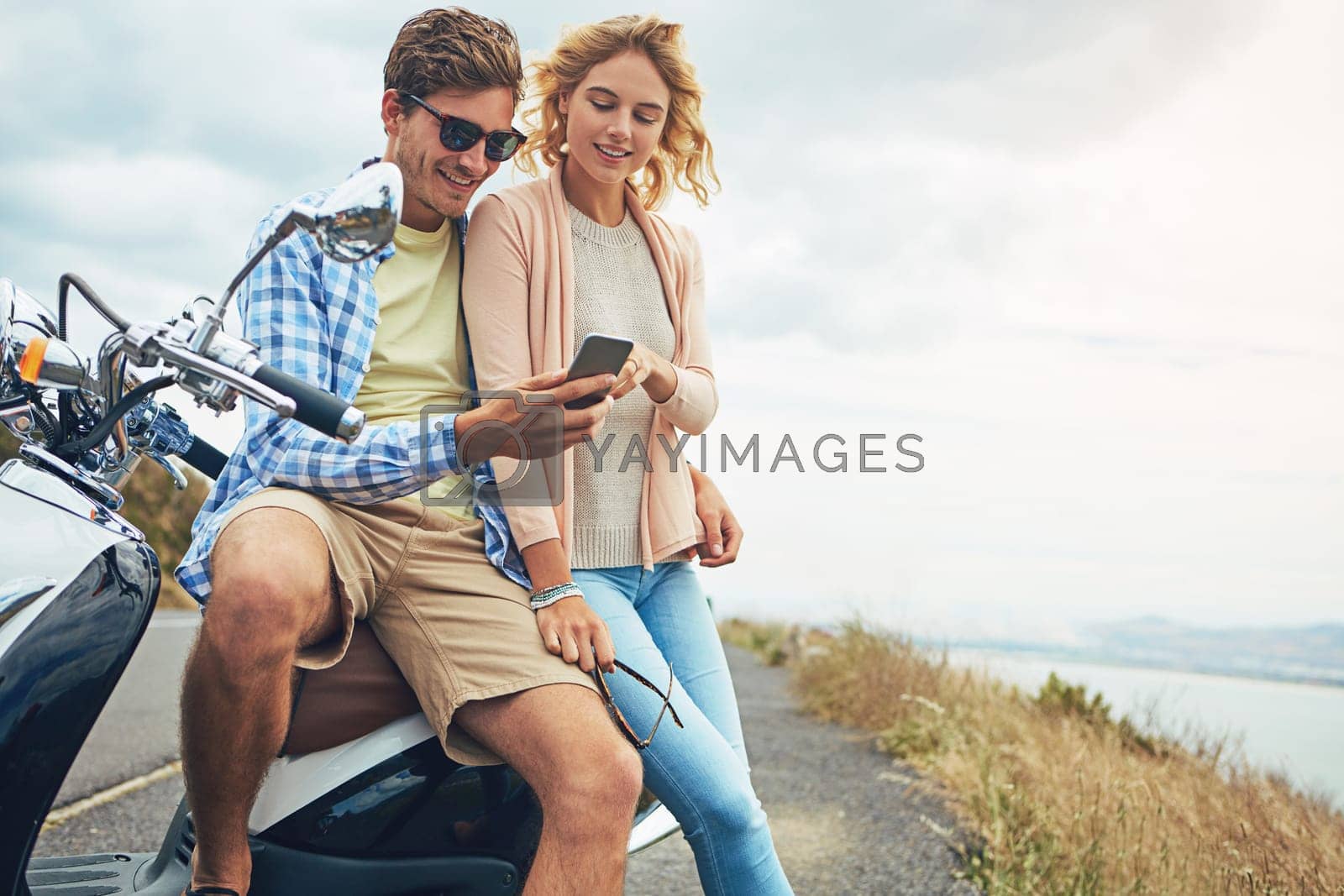 Royalty free image of Lifes a journey...why travel alone. a couple using a cellphone while taking a break from their road trip. by YuriArcurs