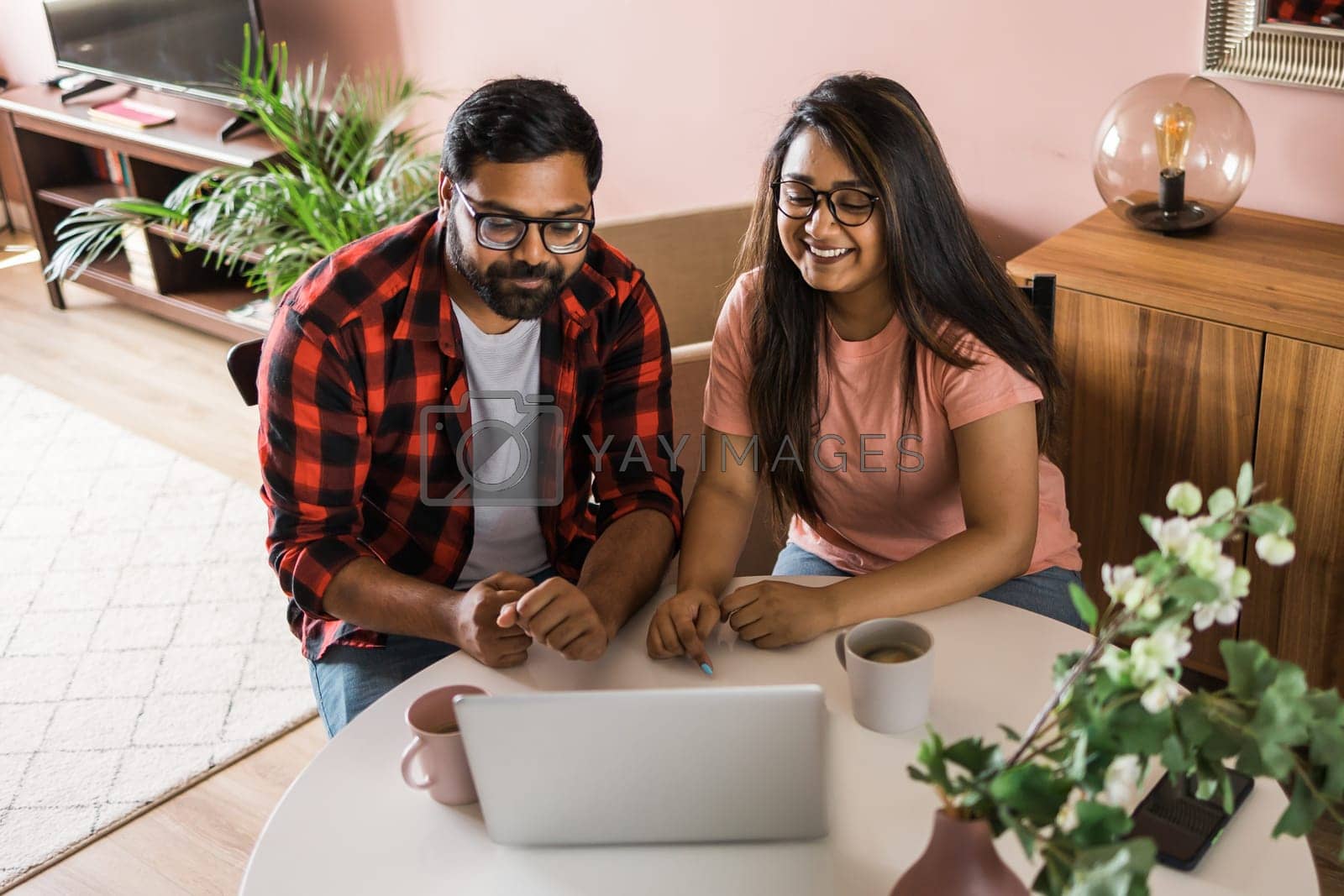 Royalty free image of Latino or indian man and woman couple use their laptop in the living room to make video calls. Video call and online chat with family by Satura86