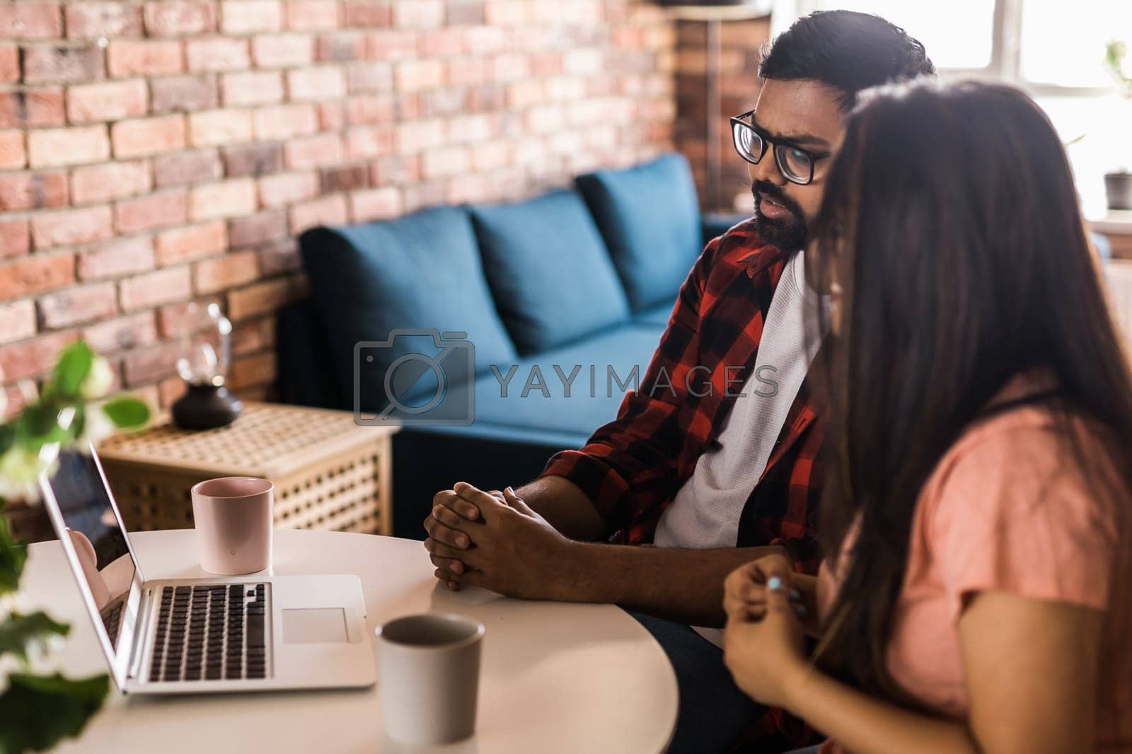 Royalty free image of Latino or indian man and woman couple use their laptop in the living room to make video calls. Video call and online chat with family by Satura86