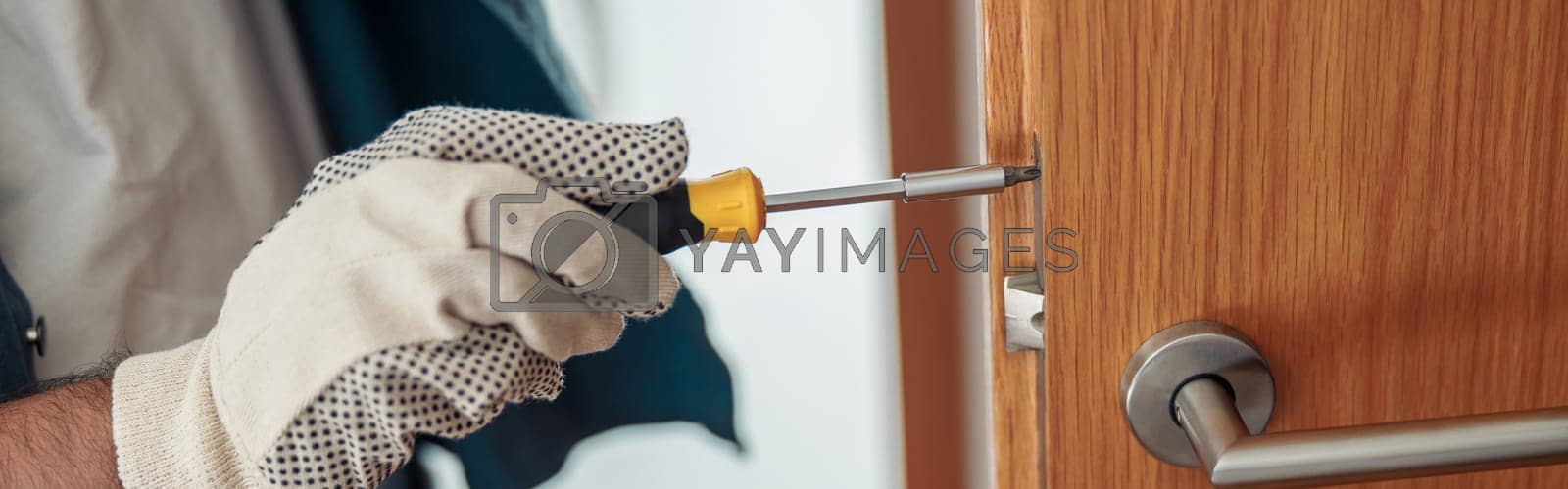 Royalty free image of Close up of locksmith workman in uniform installing door knob. Professional repair service by Yaroslav_astakhov