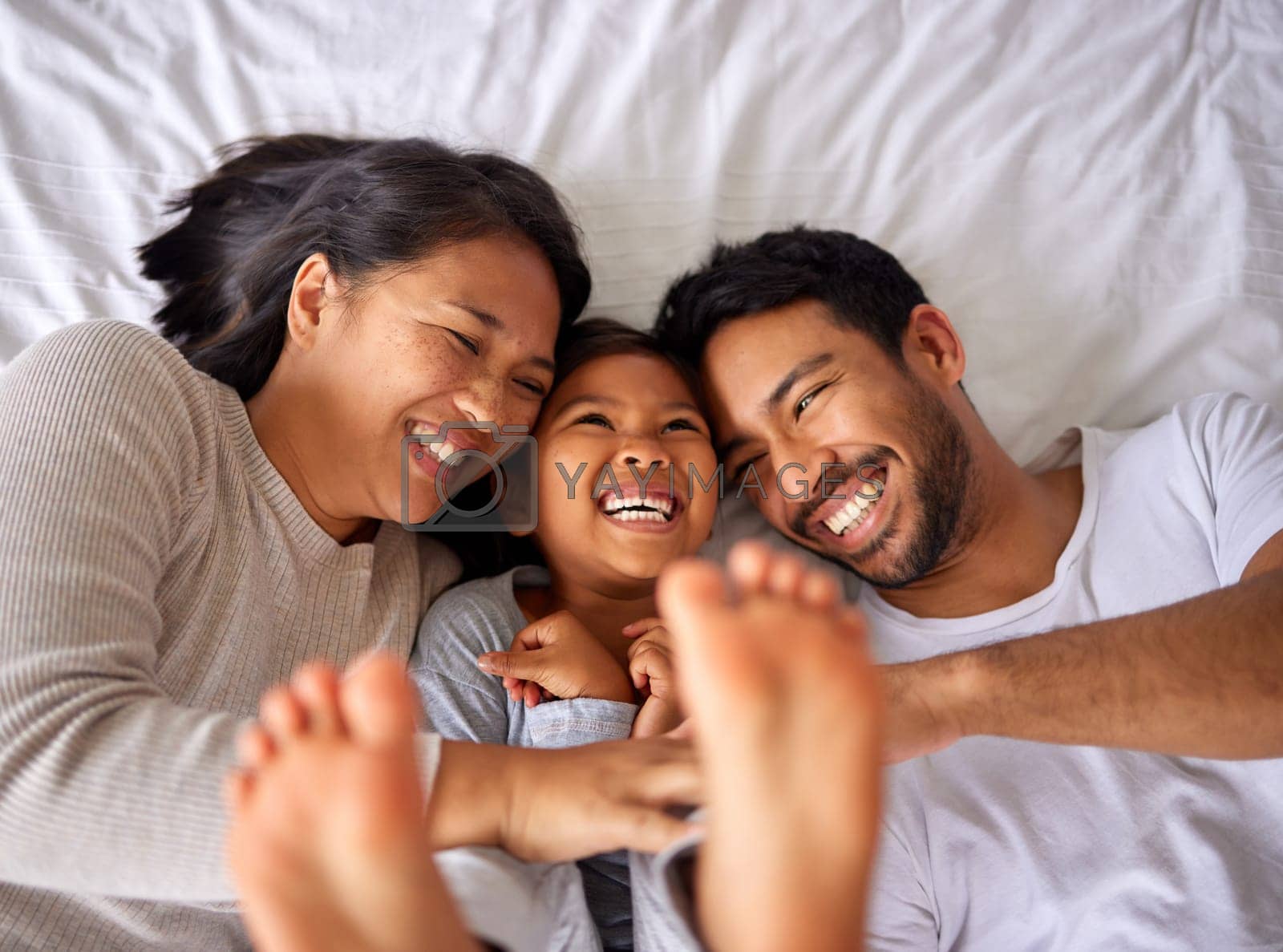 Royalty free image of Family of three laughing and having fun while lying in a bed together by YuriArcurs