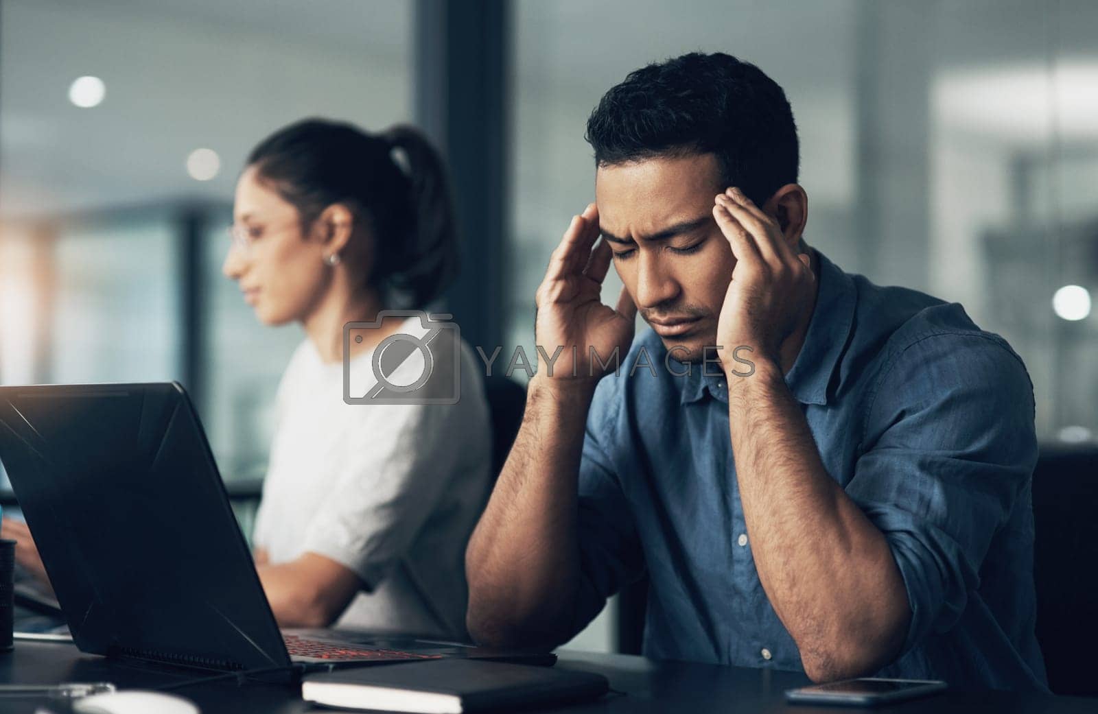 Royalty free image of Well see in the end. a young man suffering from a headache while using a laptop in a modern office. by YuriArcurs
