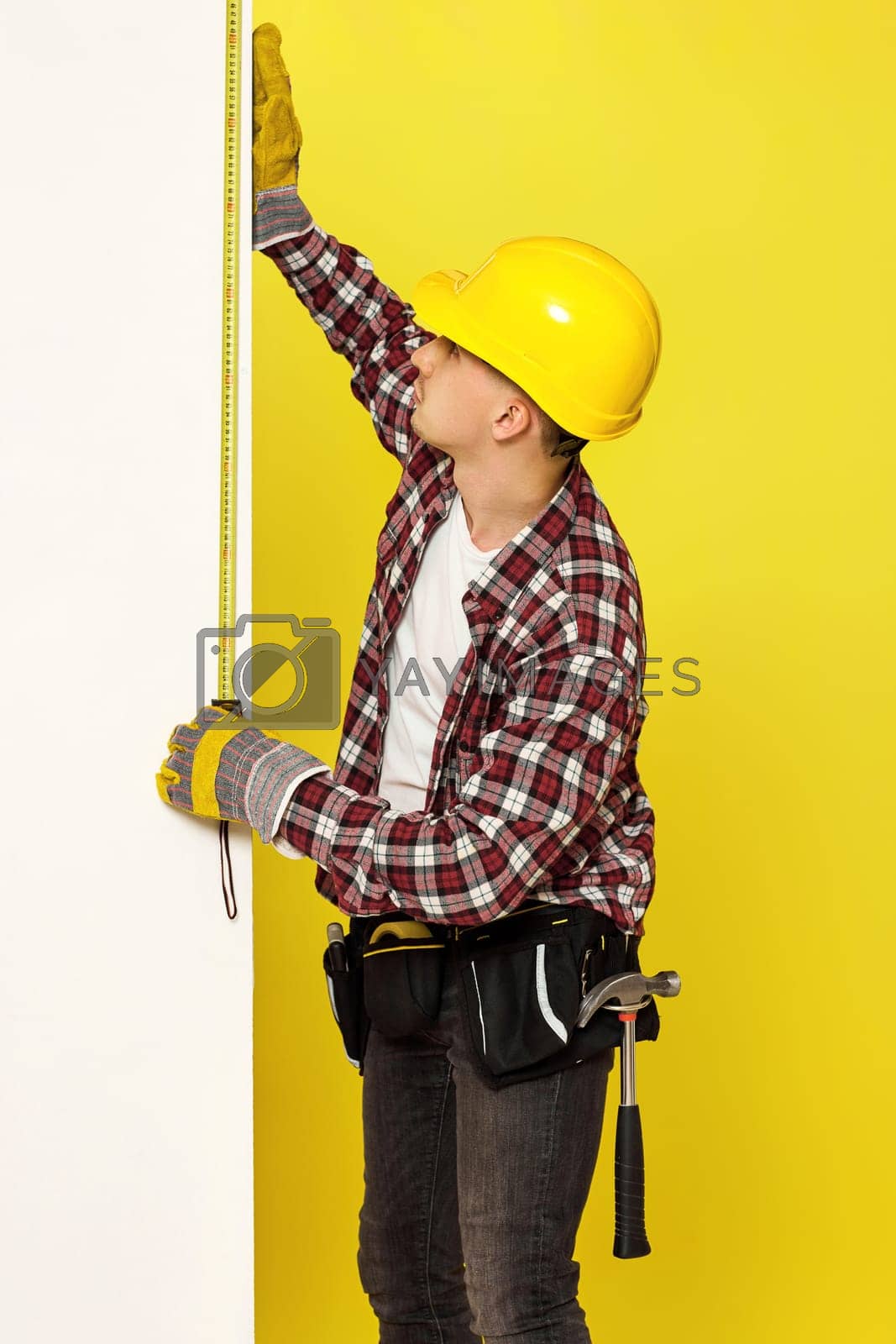 Royalty free image of builder in work clothes, helmet taking measurements of wall by erstudio