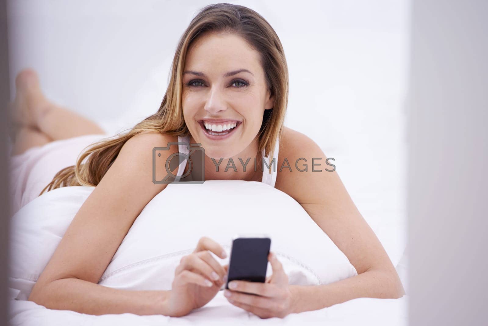 Royalty free image of Texting in the morning...Portrait of an attractive young woman reading a text message on her bed. by YuriArcurs