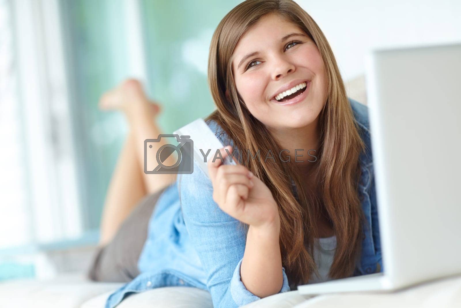 Royalty free image of Charge it to the card. A pretty teenager shopping online while relaxing on the couch. by YuriArcurs