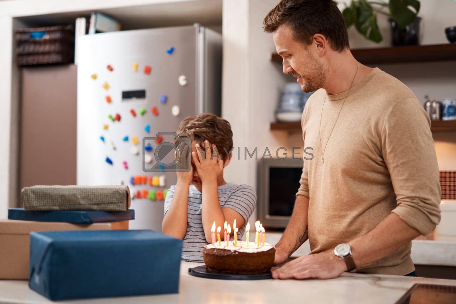 Royalty free image of Go ahead and open your eyes now. a man surprising his son with cake and gifts on his birthday. by YuriArcurs