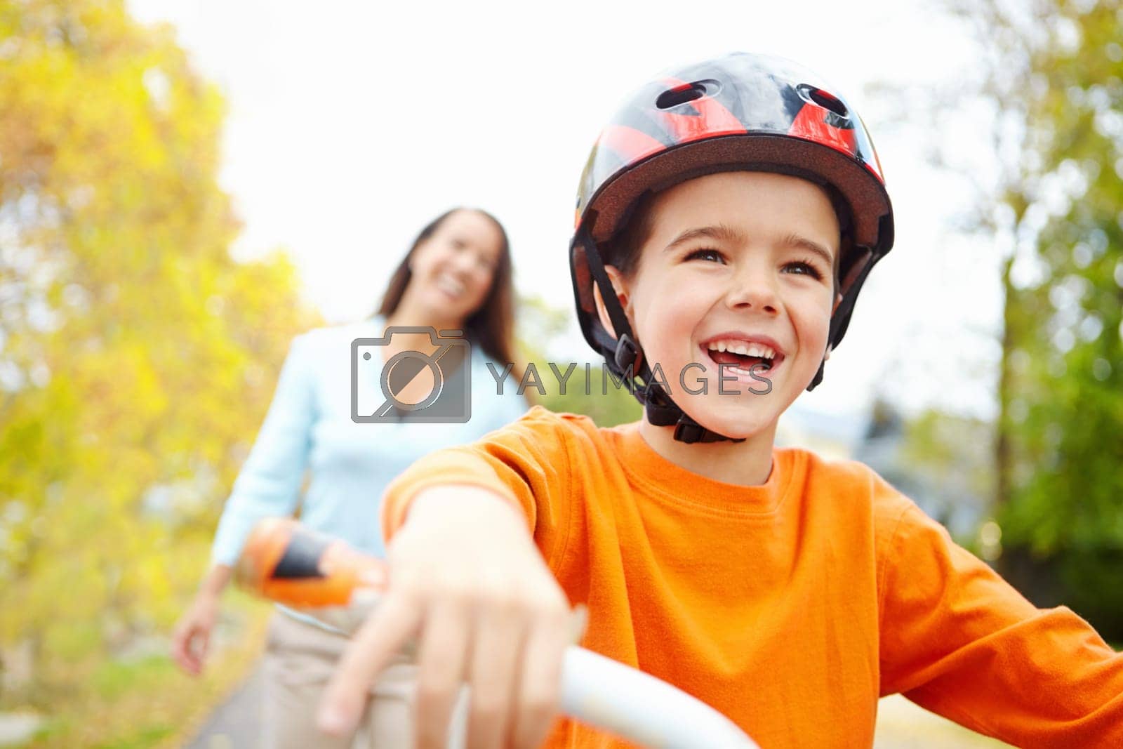 Royalty free image of Woohoo. A little boy riding a bicycle in the park with his mother standing behind him. by YuriArcurs