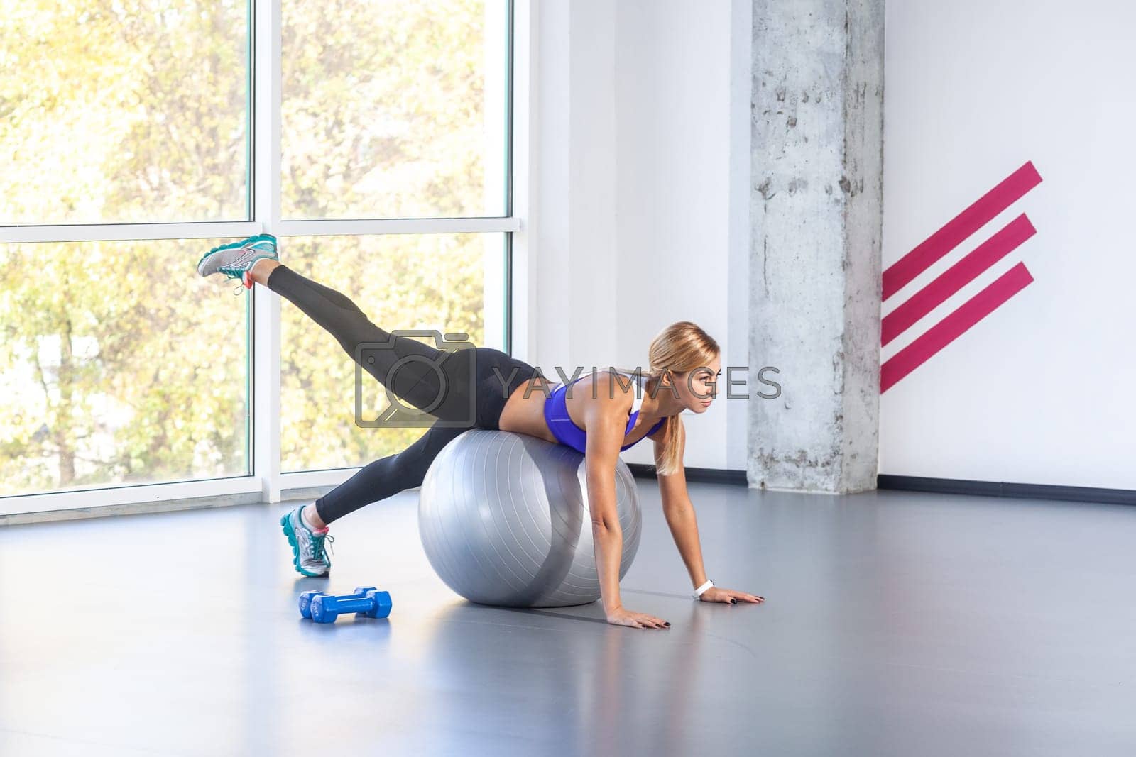Royalty free image of Woman lying on a fitness ball with palms on floor, raised her leg up, wearing sports top and tights. by Khosro1
