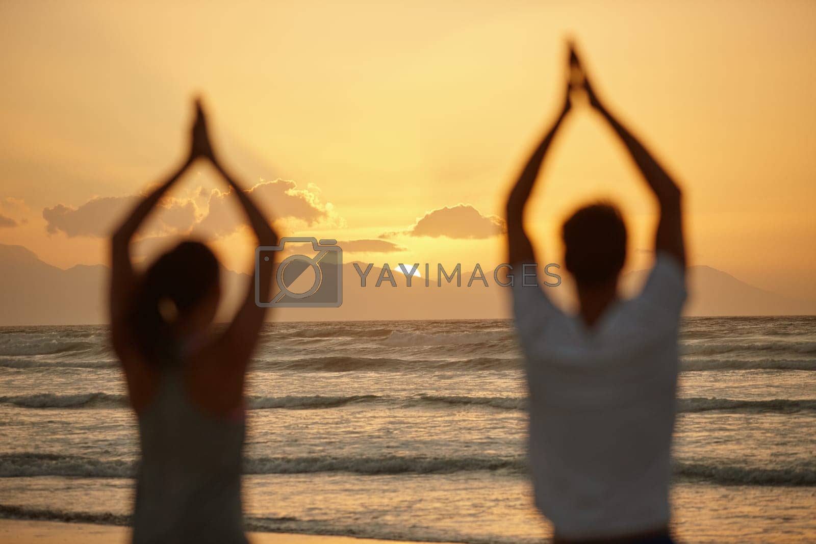 Royalty free image of Appreciating the beauty of nature while doing yoga. Rearview shot of a couple doing yoga on the beach at sunset. by YuriArcurs