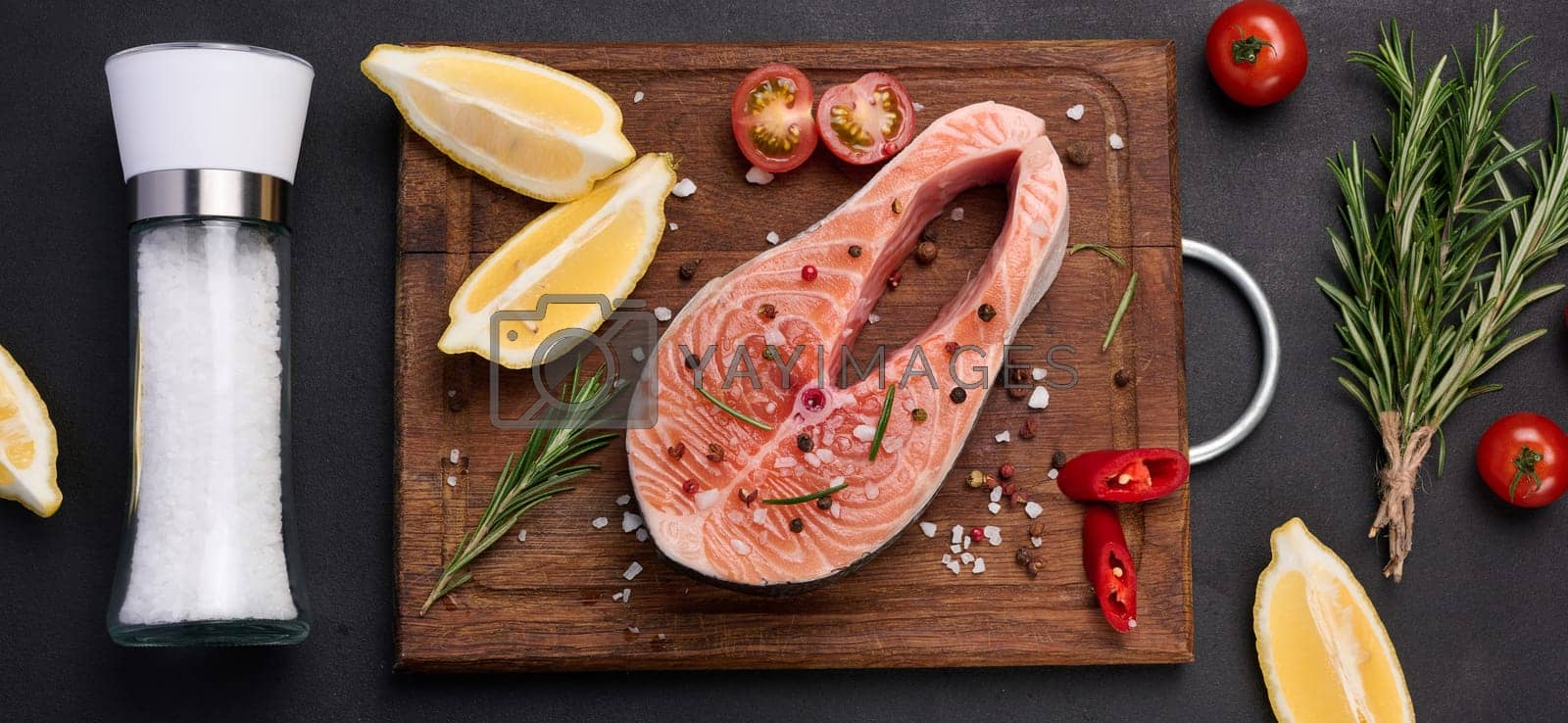 Royalty free image of Raw salmon steak on a wooden cutting board, lemon slices, spices. Top view on black table by ndanko