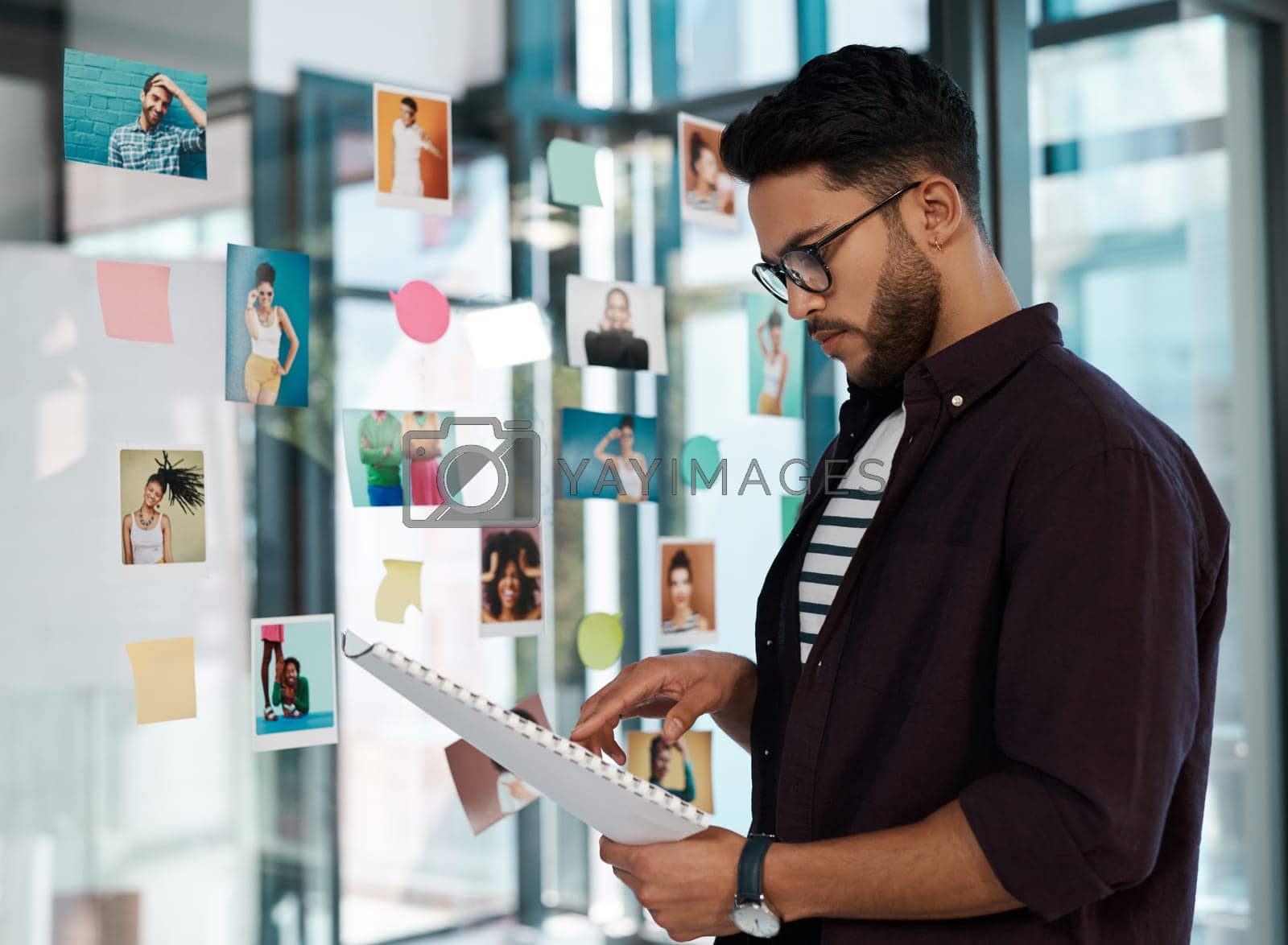 Royalty free image of Double checking I have all the polaroids. a handsome young businessman wearing spectacles and standing alone in his office while reading paperwork. by YuriArcurs