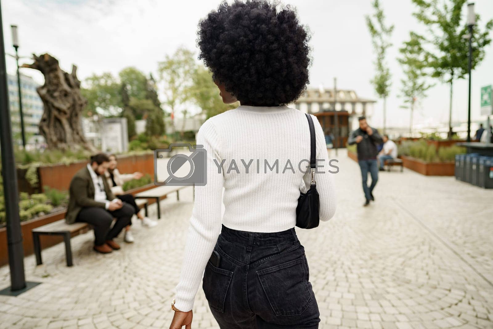 Royalty free image of Back view of african woman walking in city by Fabrikasimf