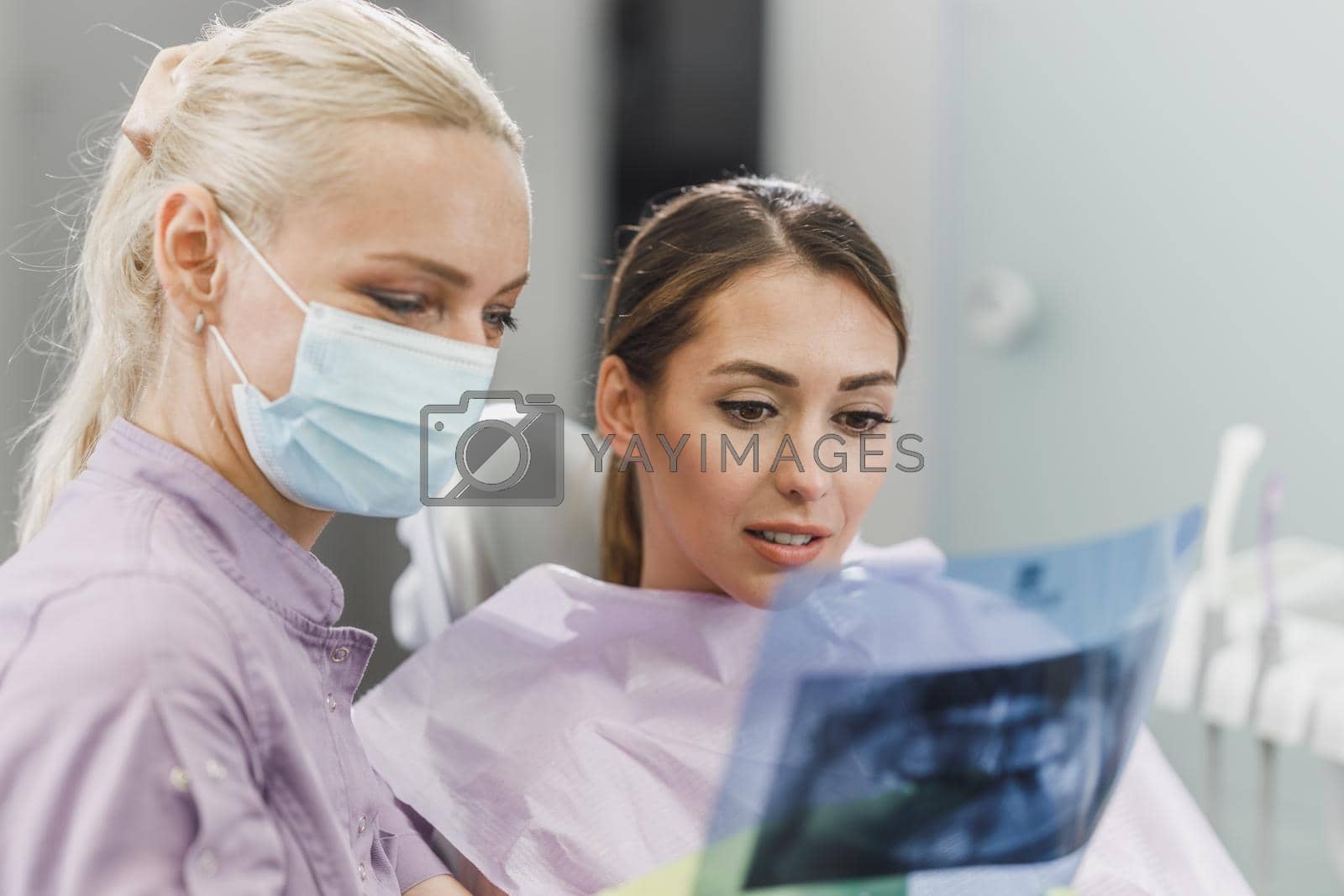A young dentist and her female patient looking at orthopantomogram during dental appointment.