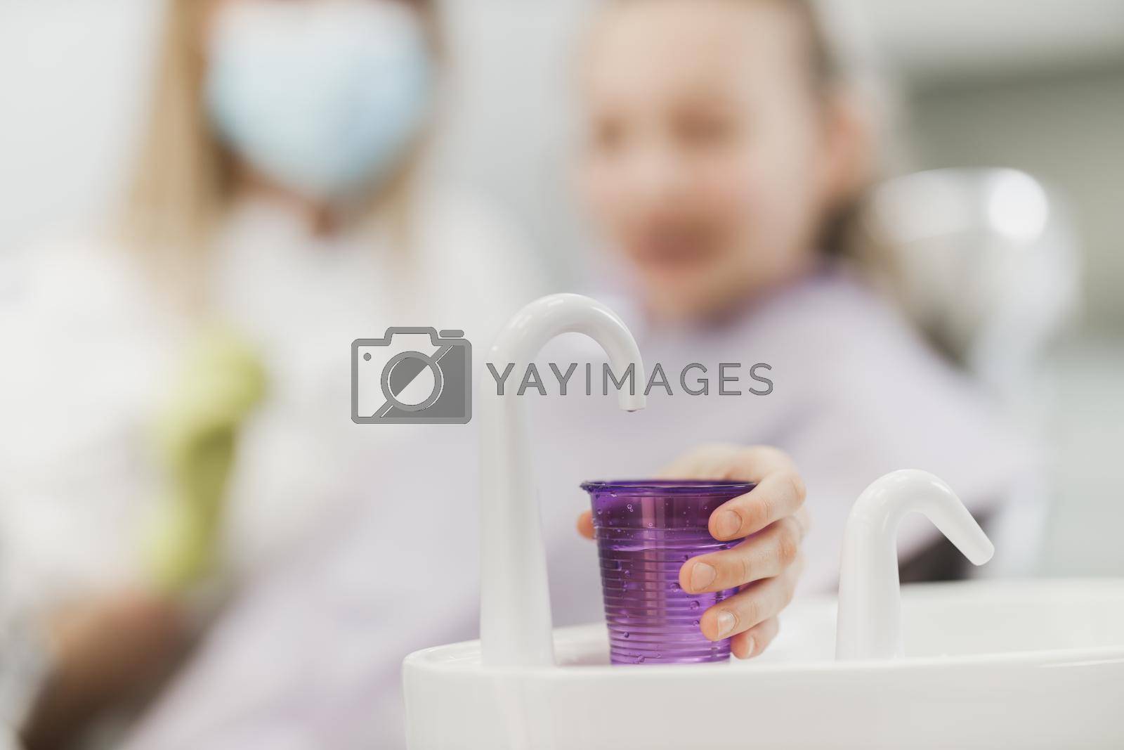 Close-up of a teenager girl  holding disposable water cup for mouthwash at the dentist. 