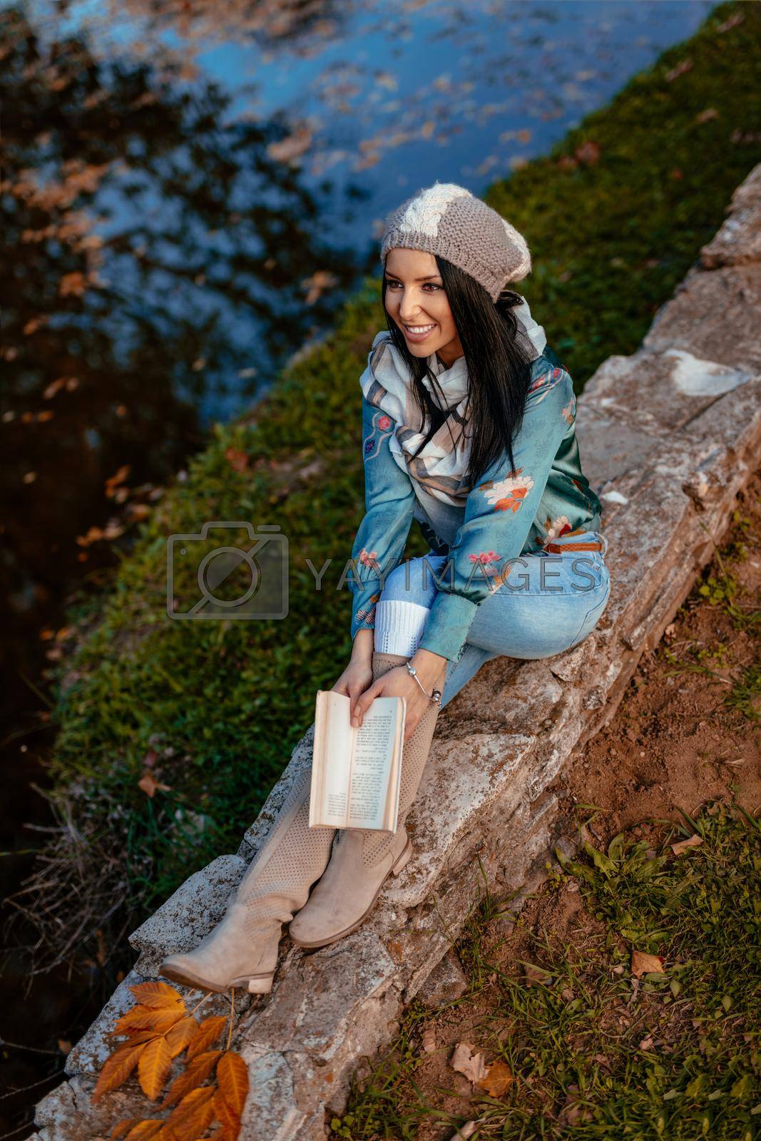 Top view of beautiful young woman enjoying in autumn colors sunny forest looking away and holding a book in her hand.  