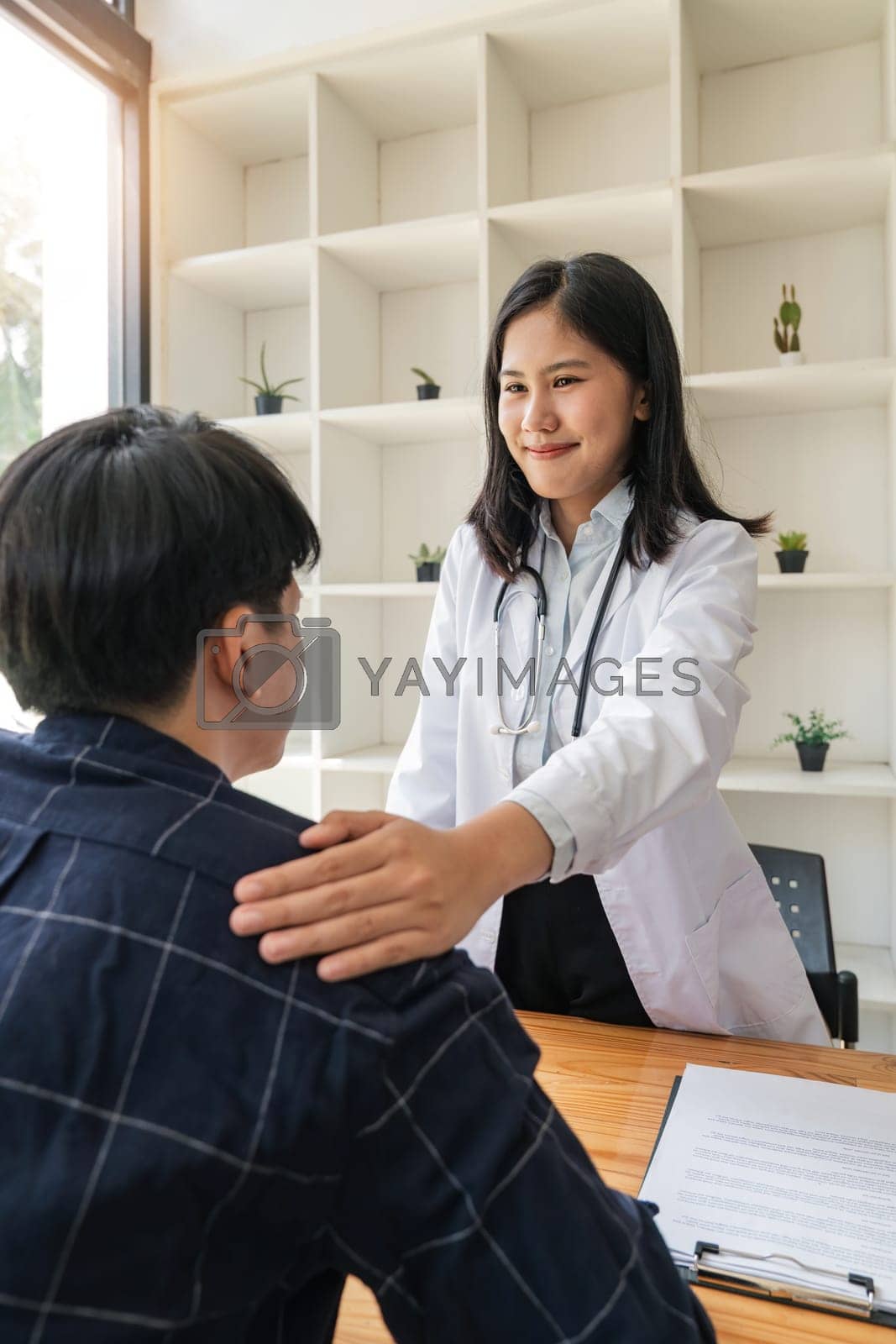 Royalty free image of Asian female doctor giving hope and encourage to stressed man patient at hospital. Smiling doctor woman touching on patient shoulder to support take care and helping . Supported and Encouraged by nateemee