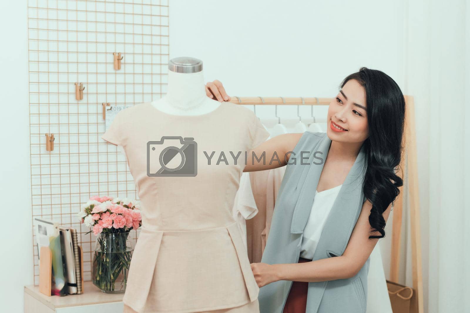 Royalty free image of An Asian girl  is working in the workshop studio. She makes fitting on the dress on the mannequin. by makidotvn
